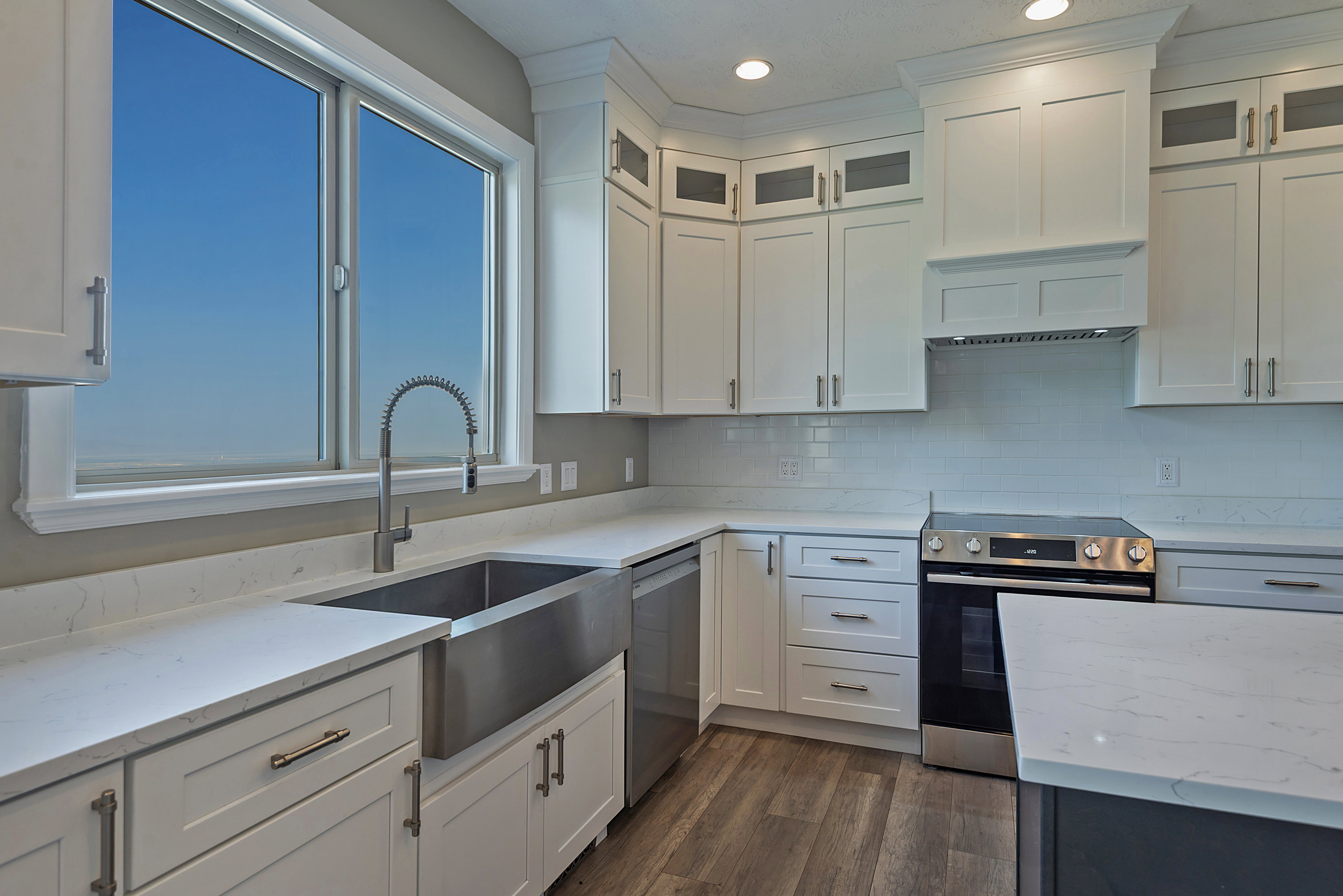 Modern kitchen featuring white cabinetry, light-toned countertops, a stainless steel farmhouse sink, and a stainless steel range with a coordinating range hood