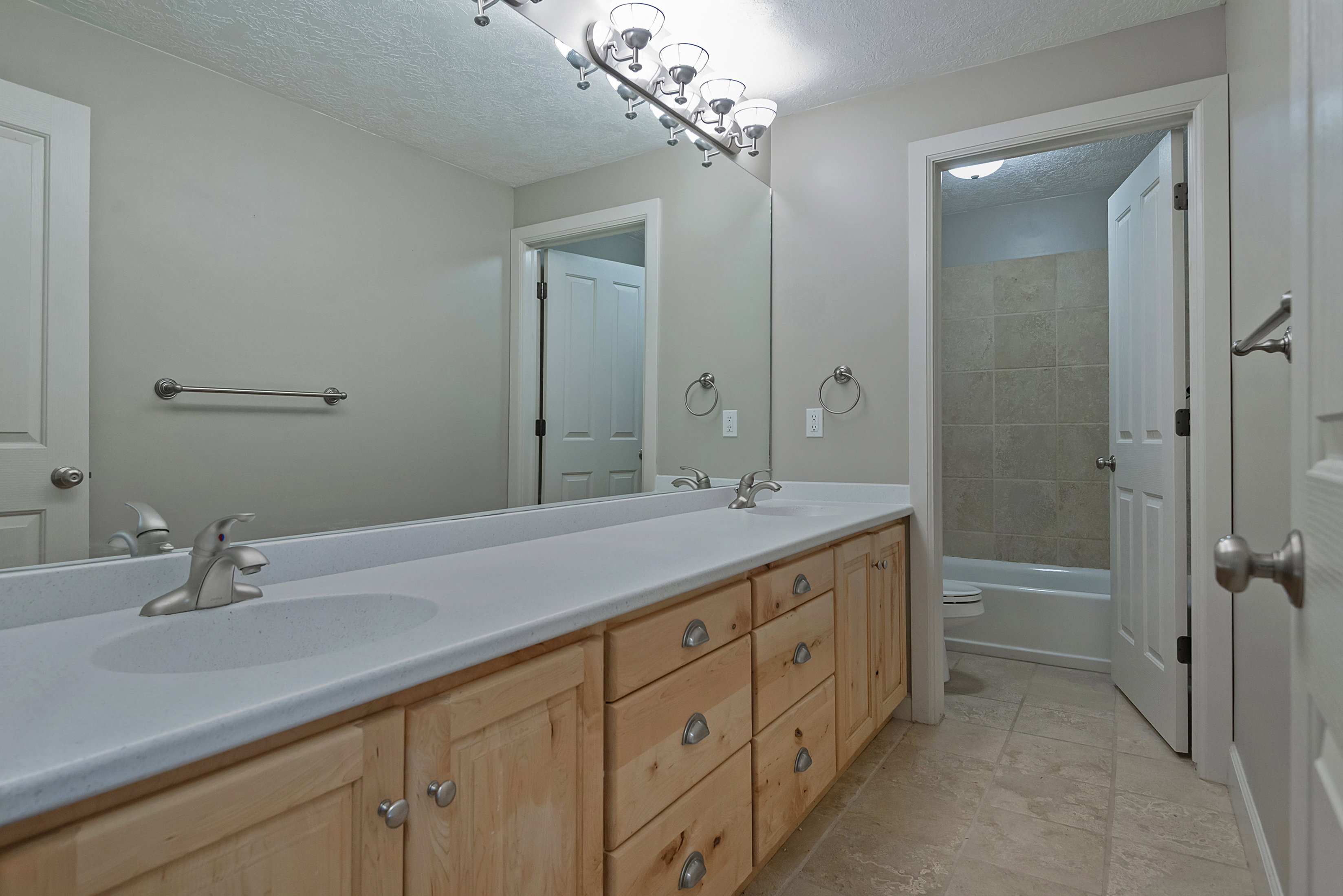 Bathroom featuring a dual vanity with light wood-finish cabinetry and a single-piece countertop with integrated sinks