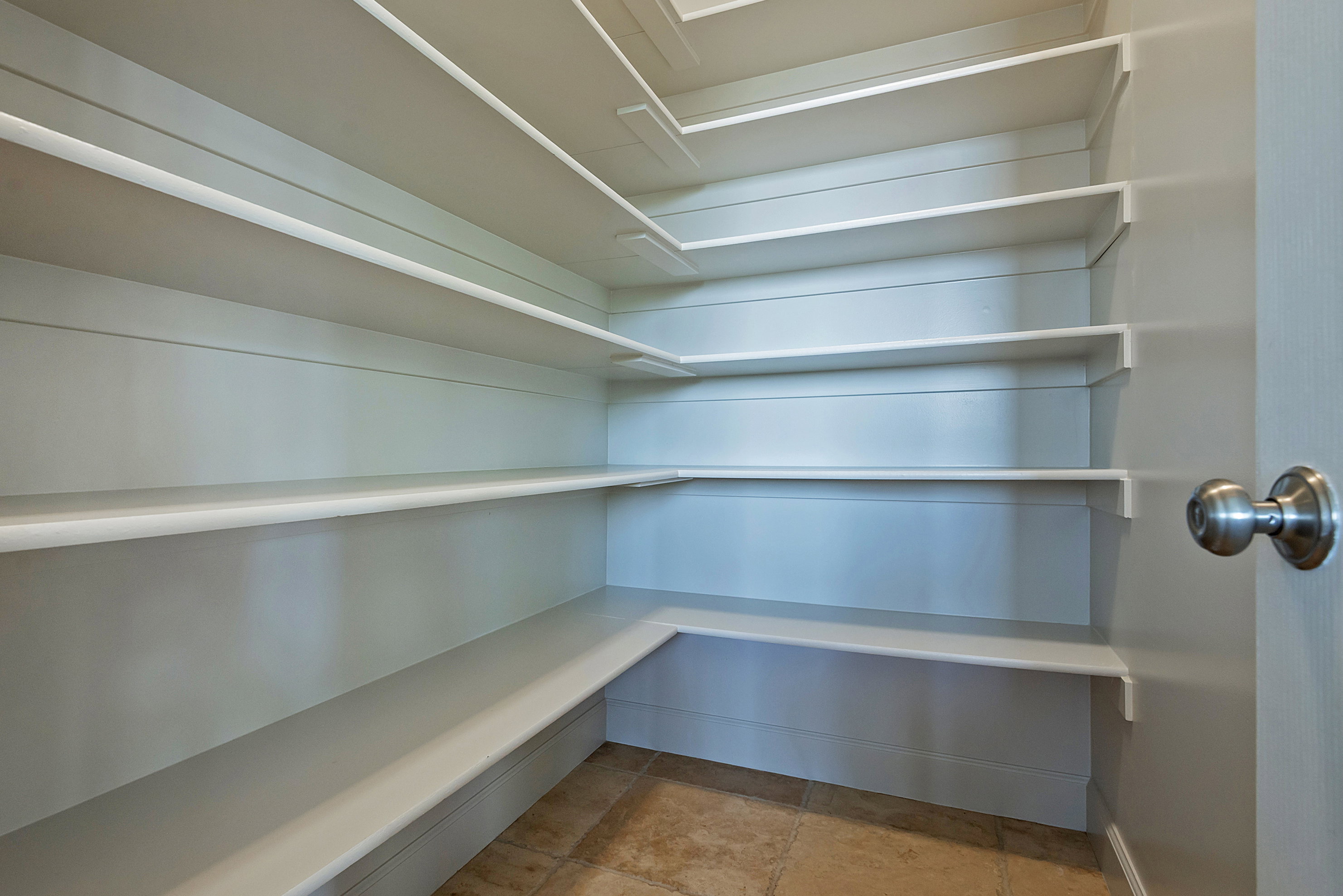 Walk-in pantry featuring multiple levels of white shelving, plank-style wall paneling, and tile flooring