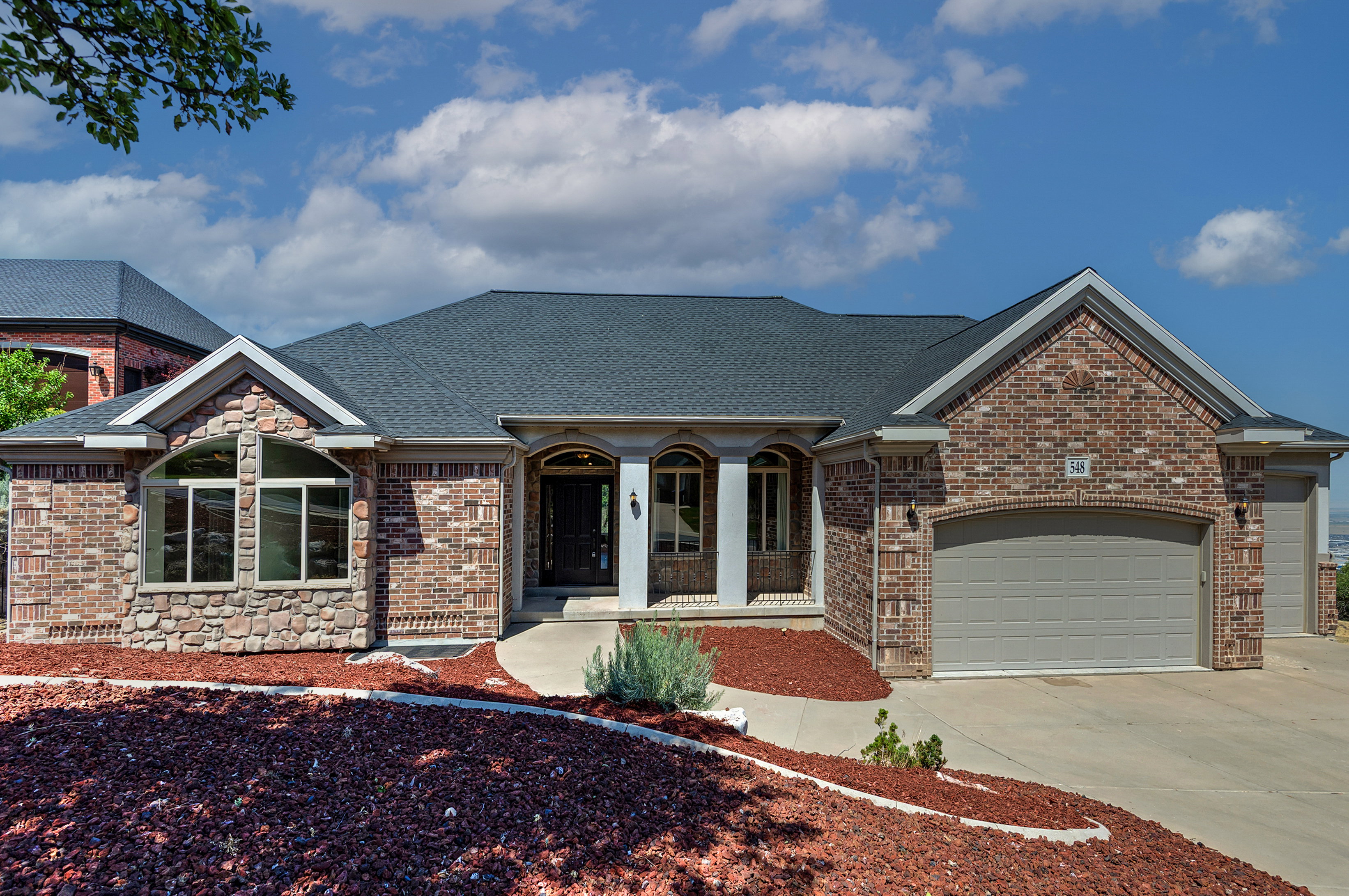 Brick and stone facade residence featuring a dark shingle roof, arched entry with columns, and a two-car garage