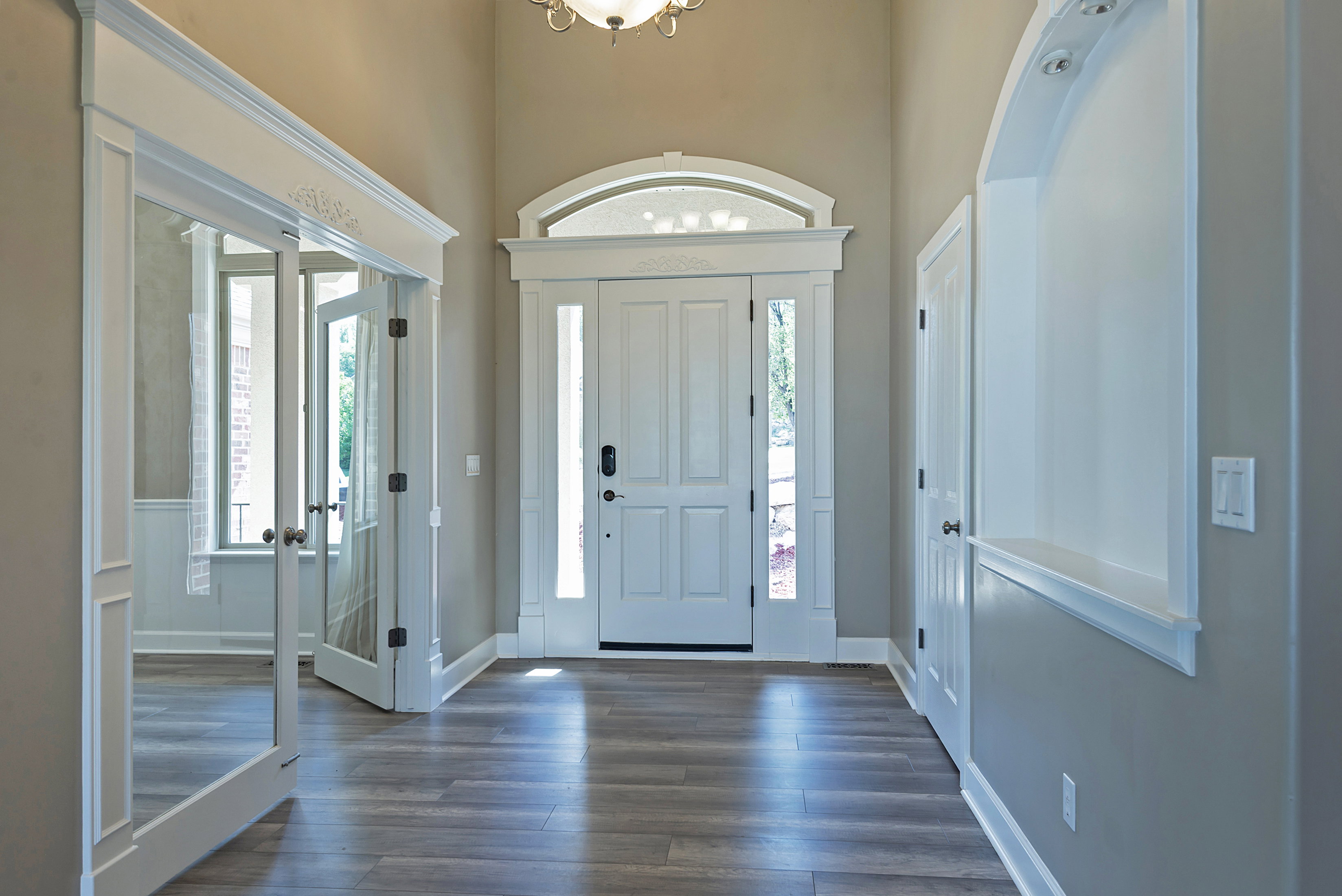 Foyer featuring wood-finish flooring, a double-door entry with sidelights and an arched transom, a decorative built-in niche with accent lighting, and a chandelier