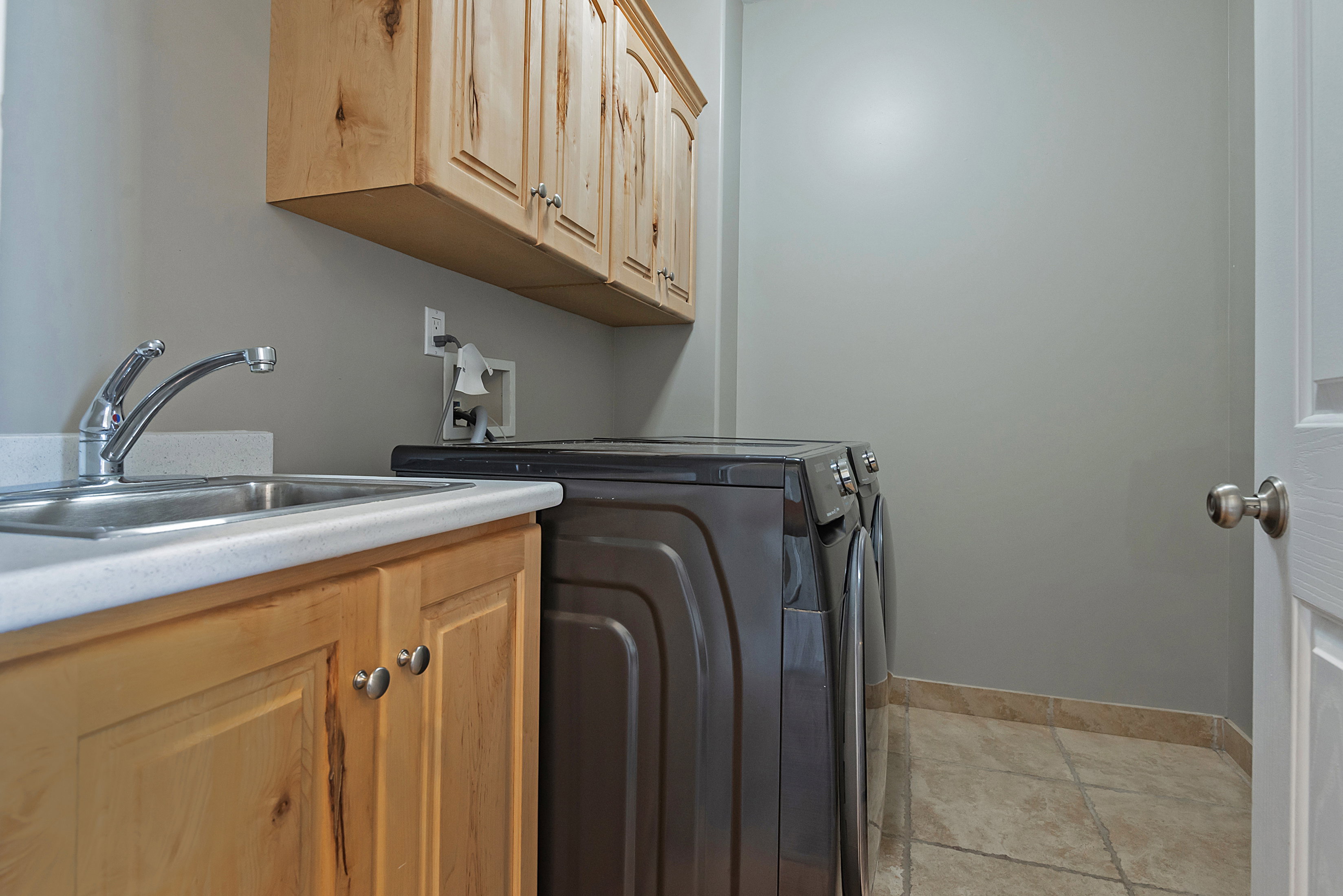 Dedicated laundry area featuring a built-in sink with a chrome faucet, light wood-finish cabinetry, and light-toned floor tiling