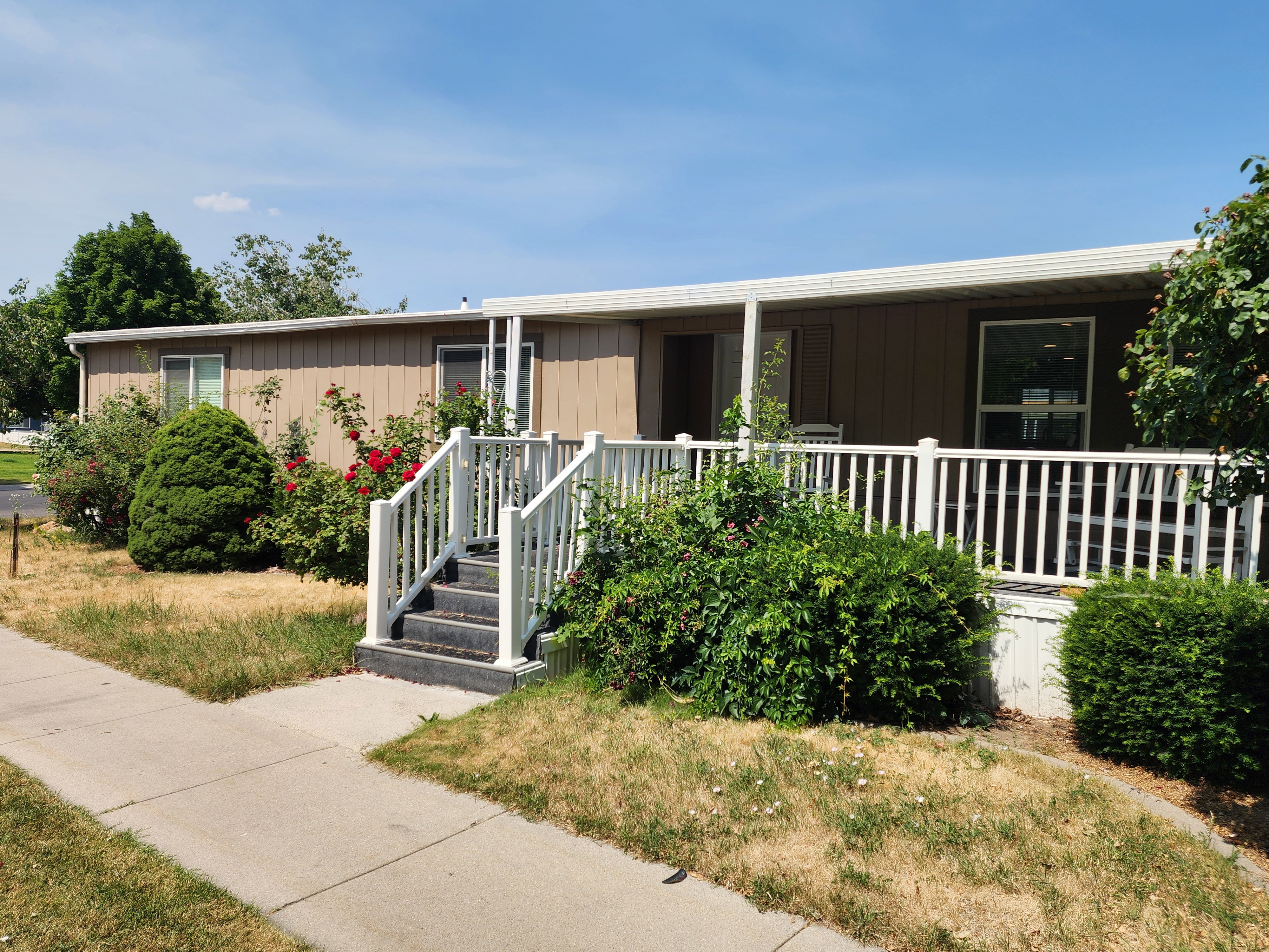Exterior featuring a covered porch with white railing, established shrubbery, red rose bushes, and a paved walkway