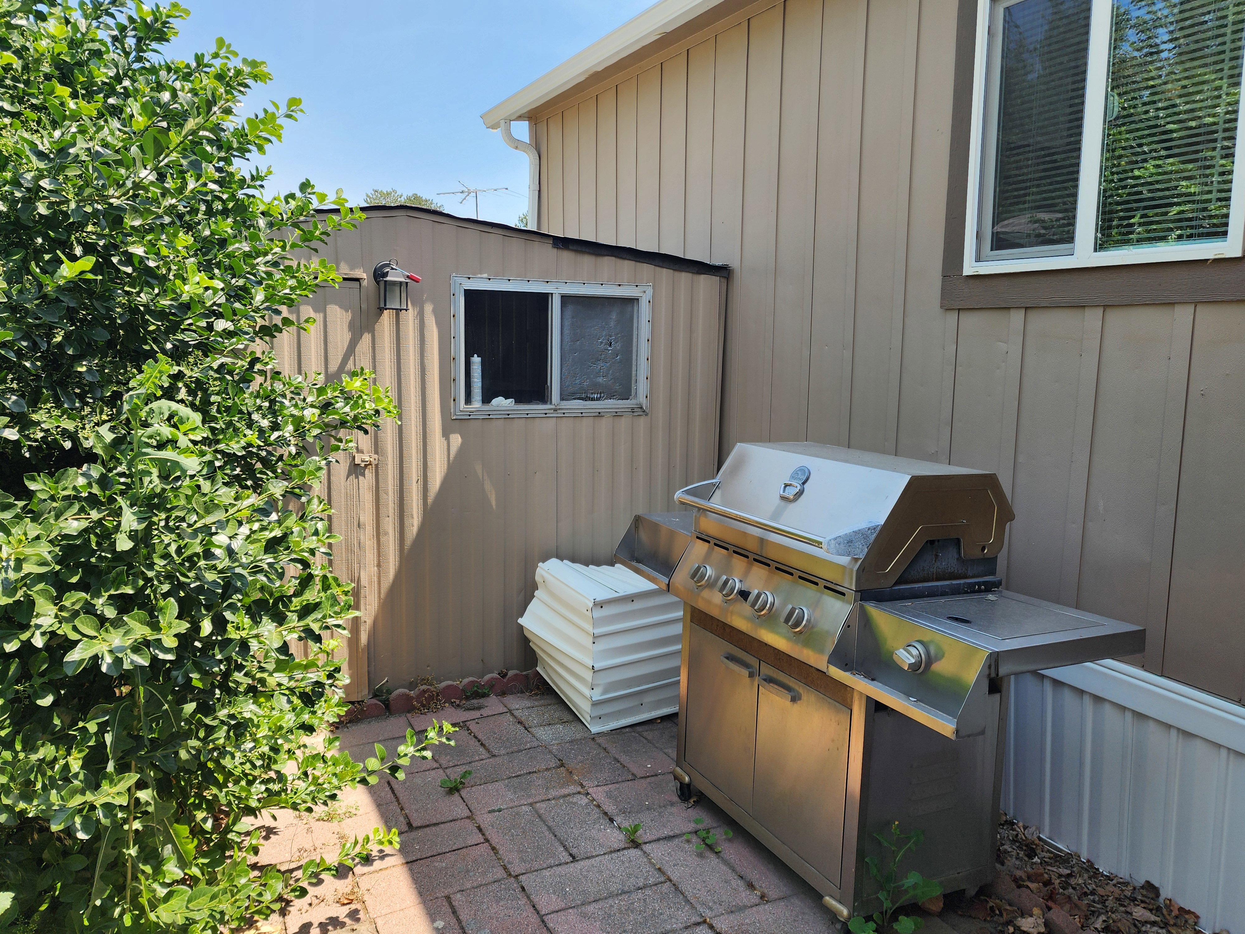 Paved patio area with brick pavers, featuring a storage shed with a window and exterior lighting
