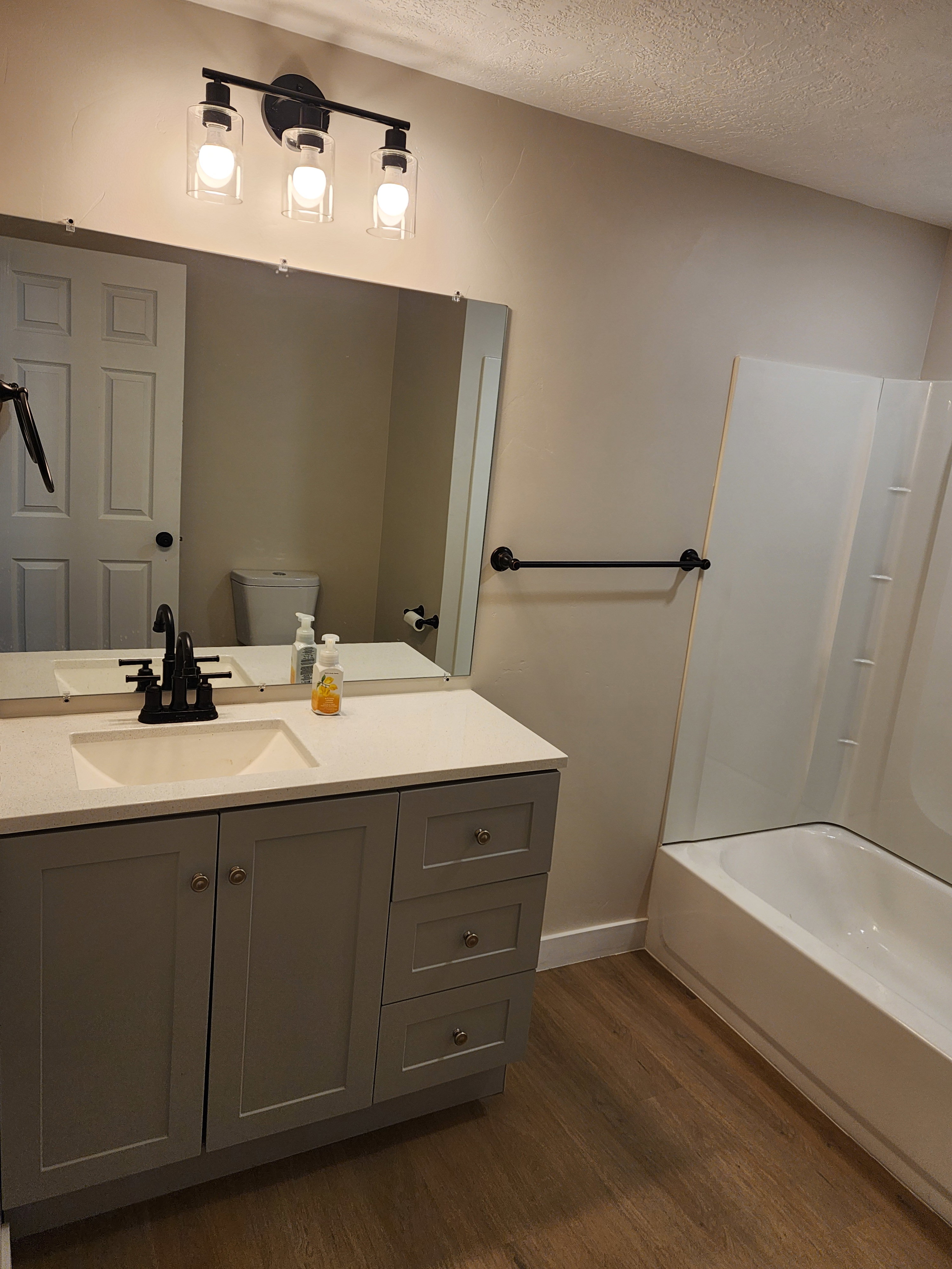 Bathroom featuring a light gray vanity with a single basin sink, light-toned countertop, and wood-finish flooring
