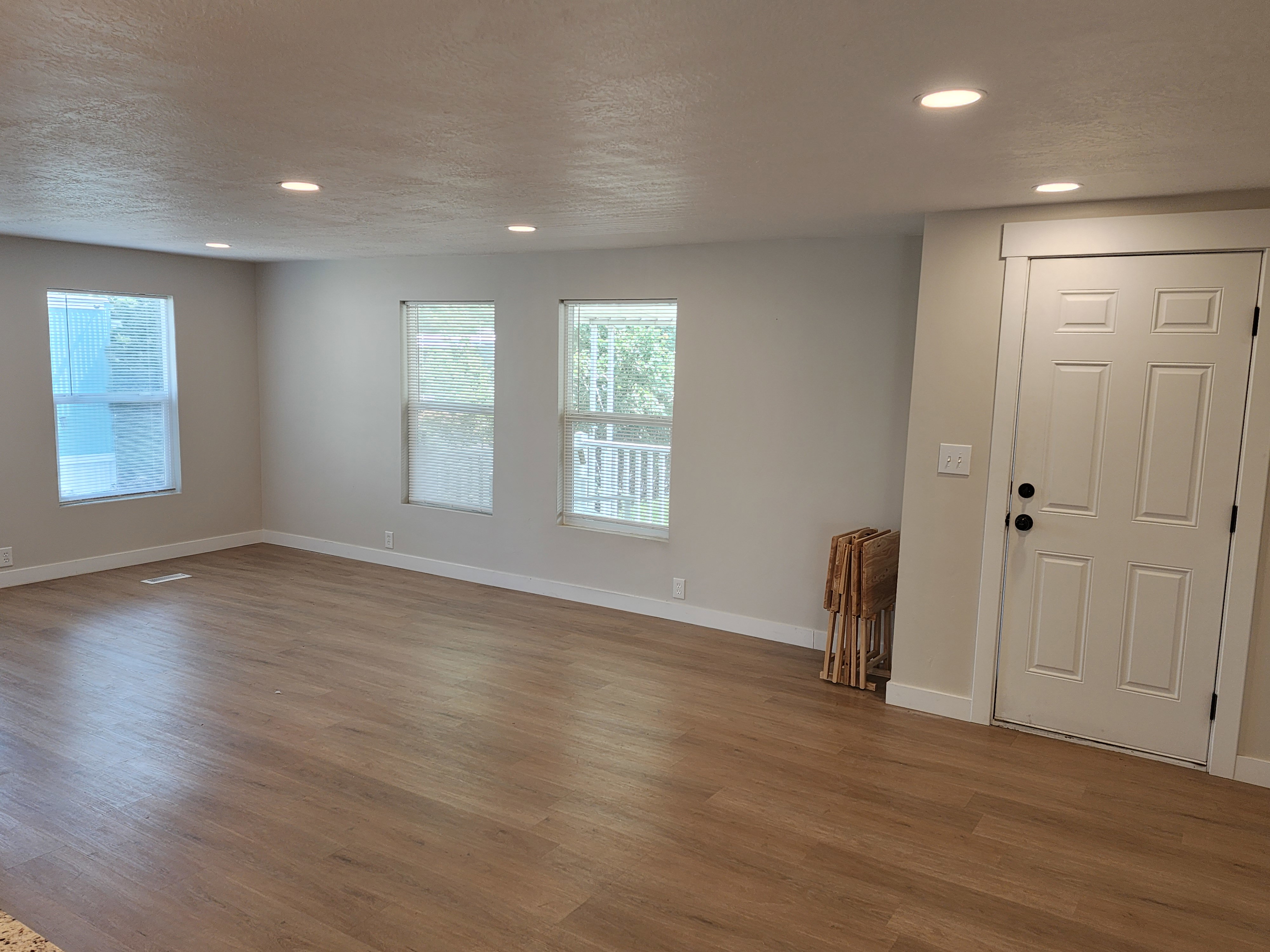 Open-concept living area featuring wood-finish flooring, recessed lighting, multiple windows, light-colored walls, and a paneled entry door with dark hardware