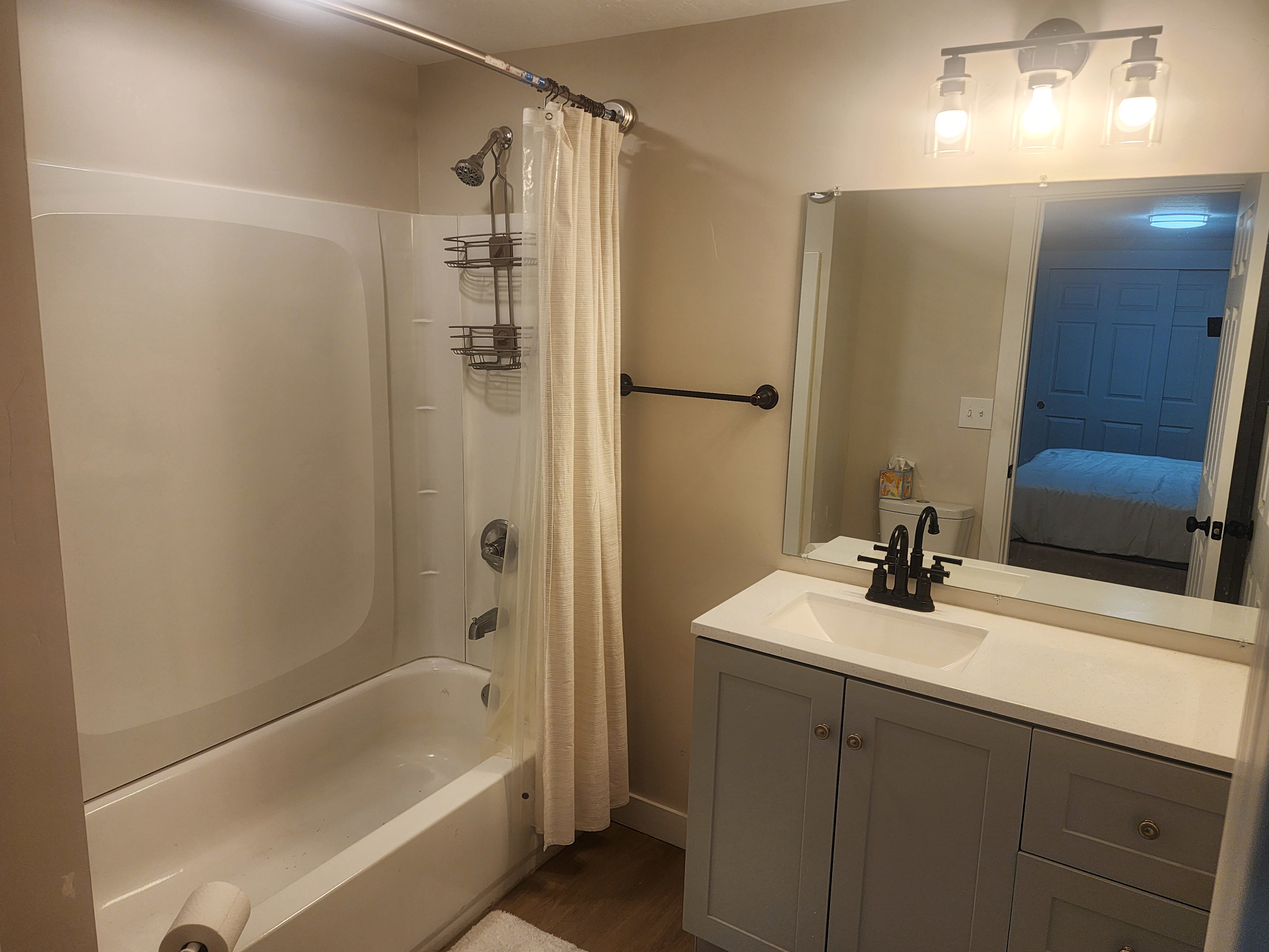 Bathroom featuring a white tub/shower combination, a vanity with a white countertop and integrated sink, a dark bronze faucet, and a wall-mounted mirror