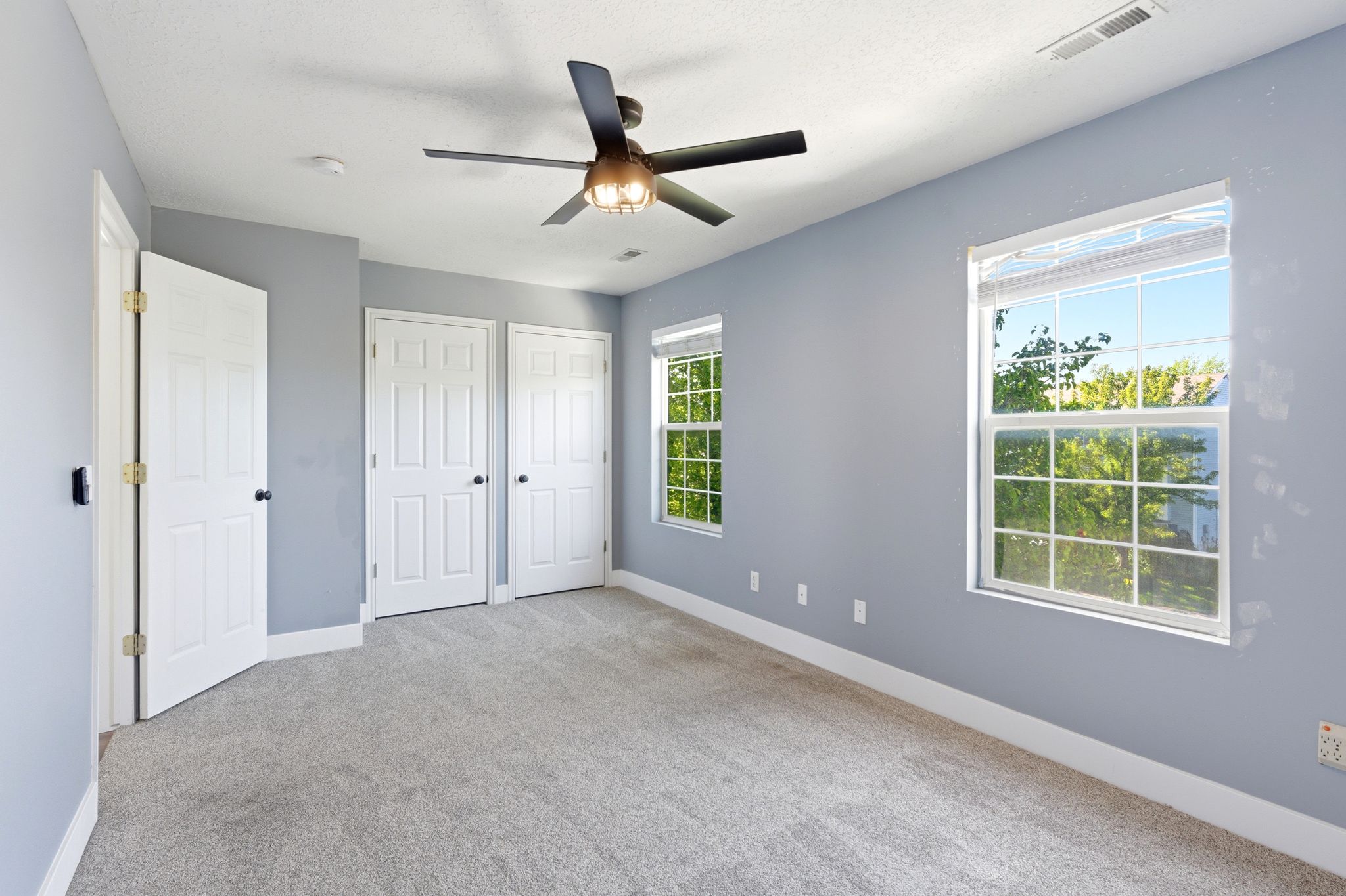 Carpeted room featuring light gray walls, two windows, and a ceiling fan with integrated lighting