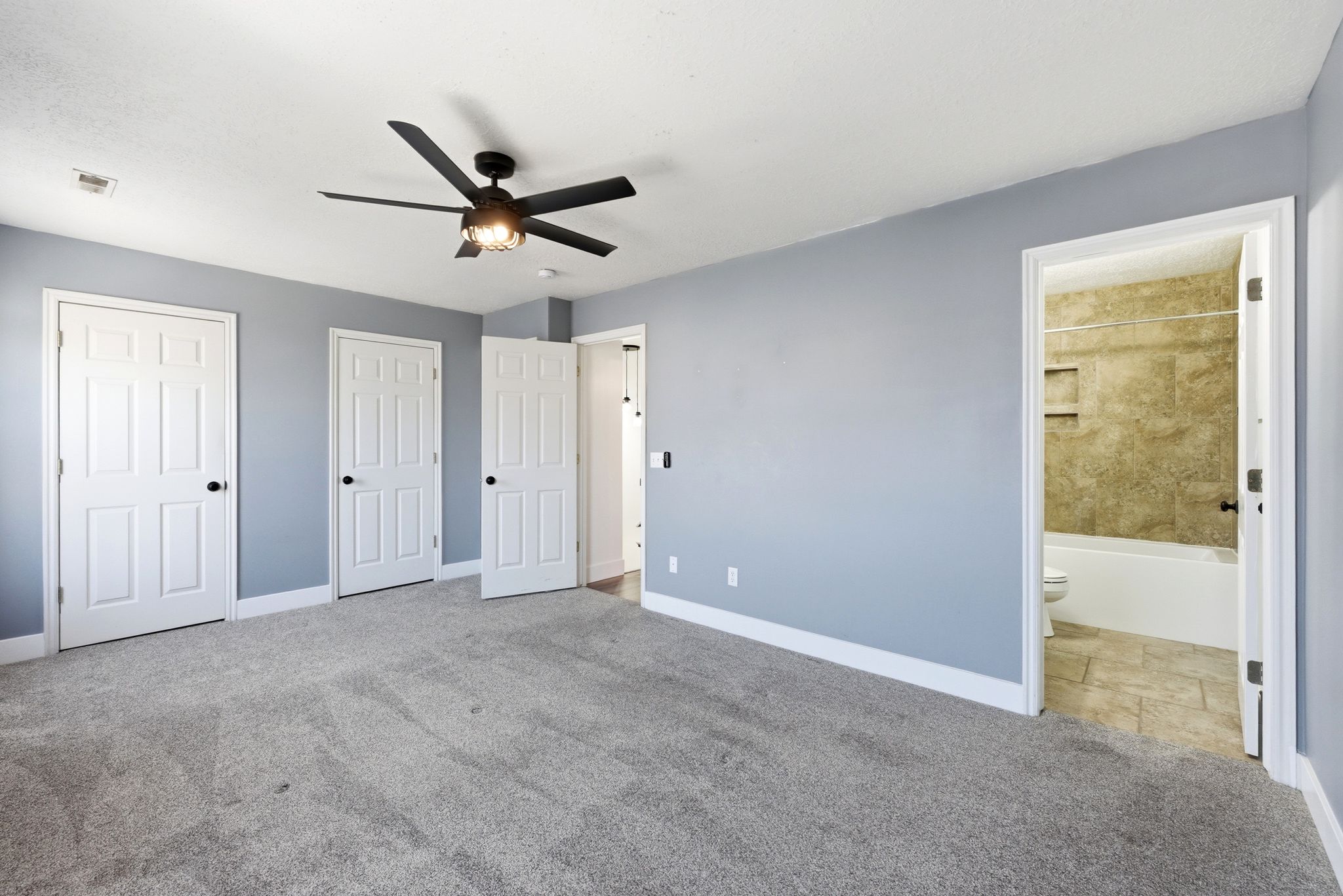 Spacious room featuring light gray carpeting, light blue walls, and a ceiling fan with integrated lighting