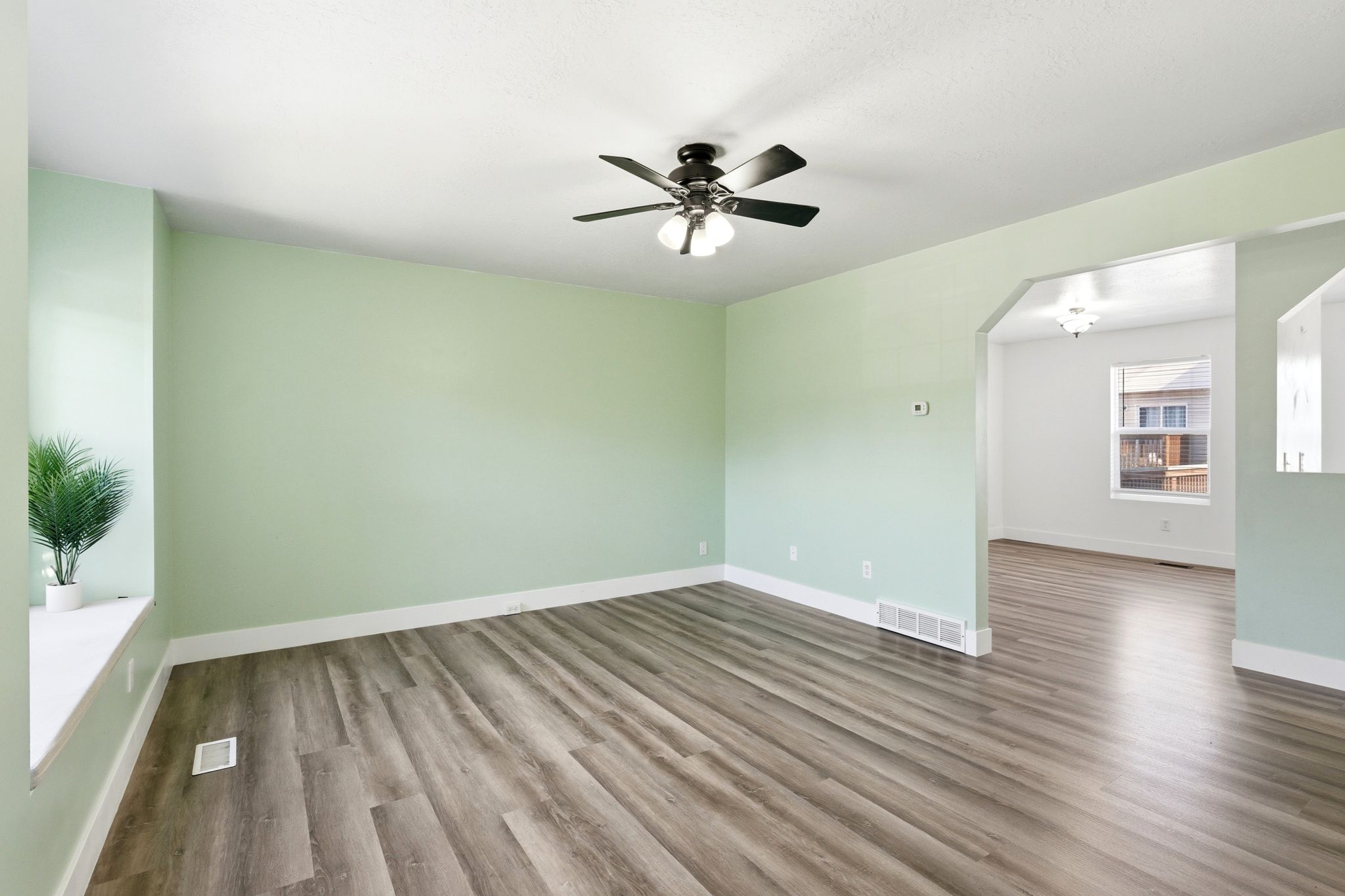 Spacious room featuring wood-finish flooring, a ceiling fan with integrated lighting, and an arched doorway opening to an additional area
