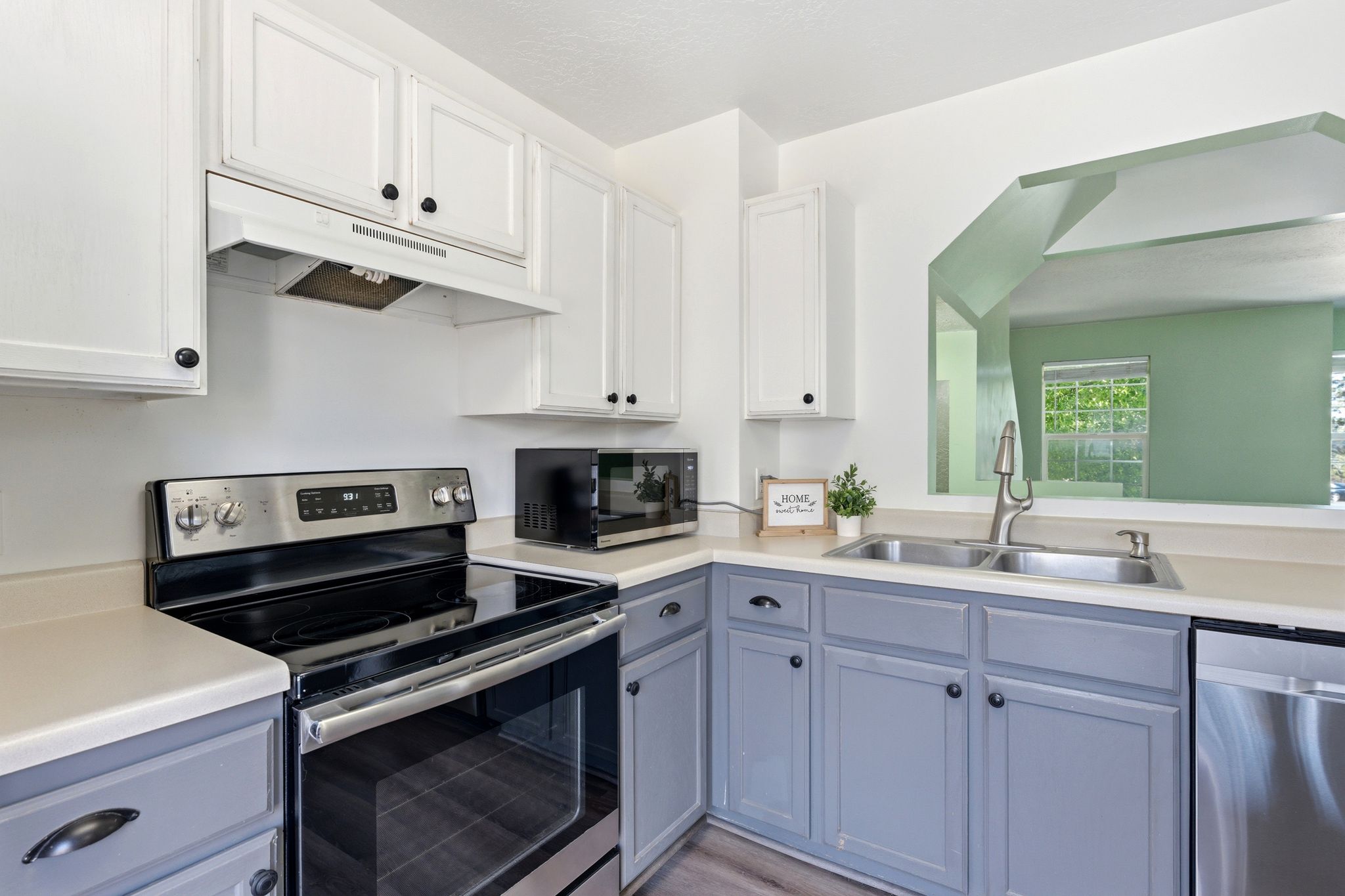 Kitchen featuring a stainless steel electric range, a double basin sink, light-toned countertops, two-tone cabinetry with black hardware, and an open pass-through window to an adjacent room