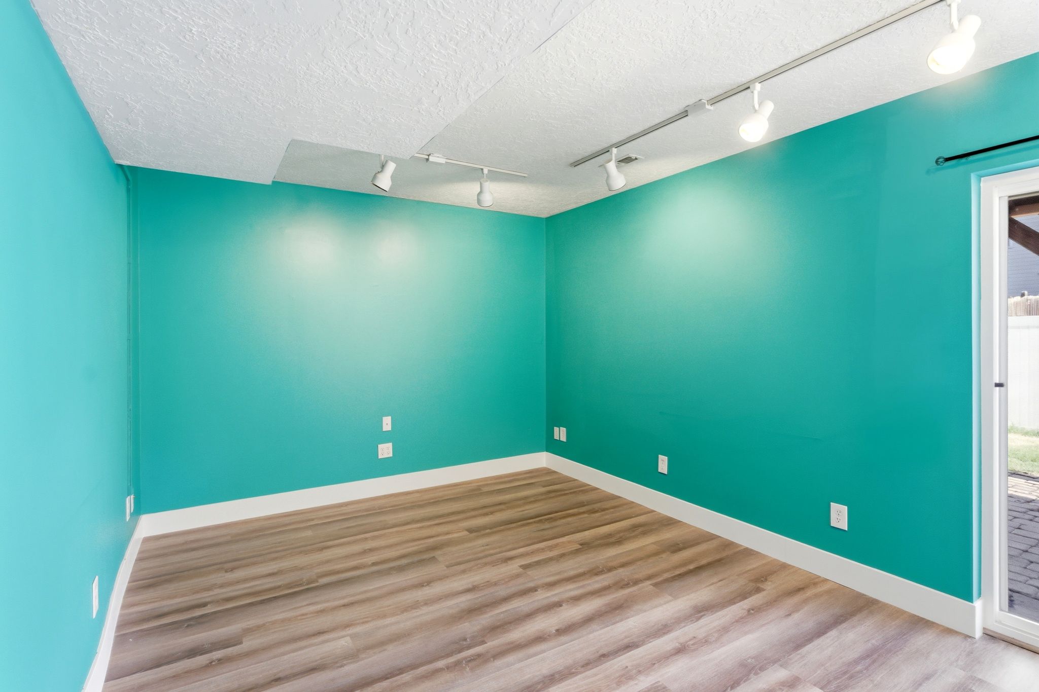 Spacious room featuring wood-finish flooring, vibrant turquoise walls, and track lighting