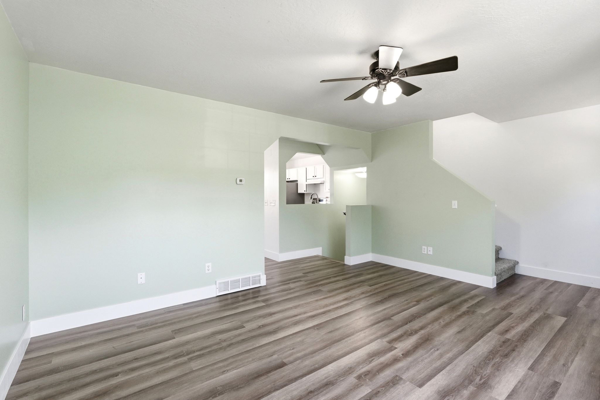 Spacious interior featuring wood-finish flooring, a ceiling fan with integrated lighting, and a staircase with carpeted treads