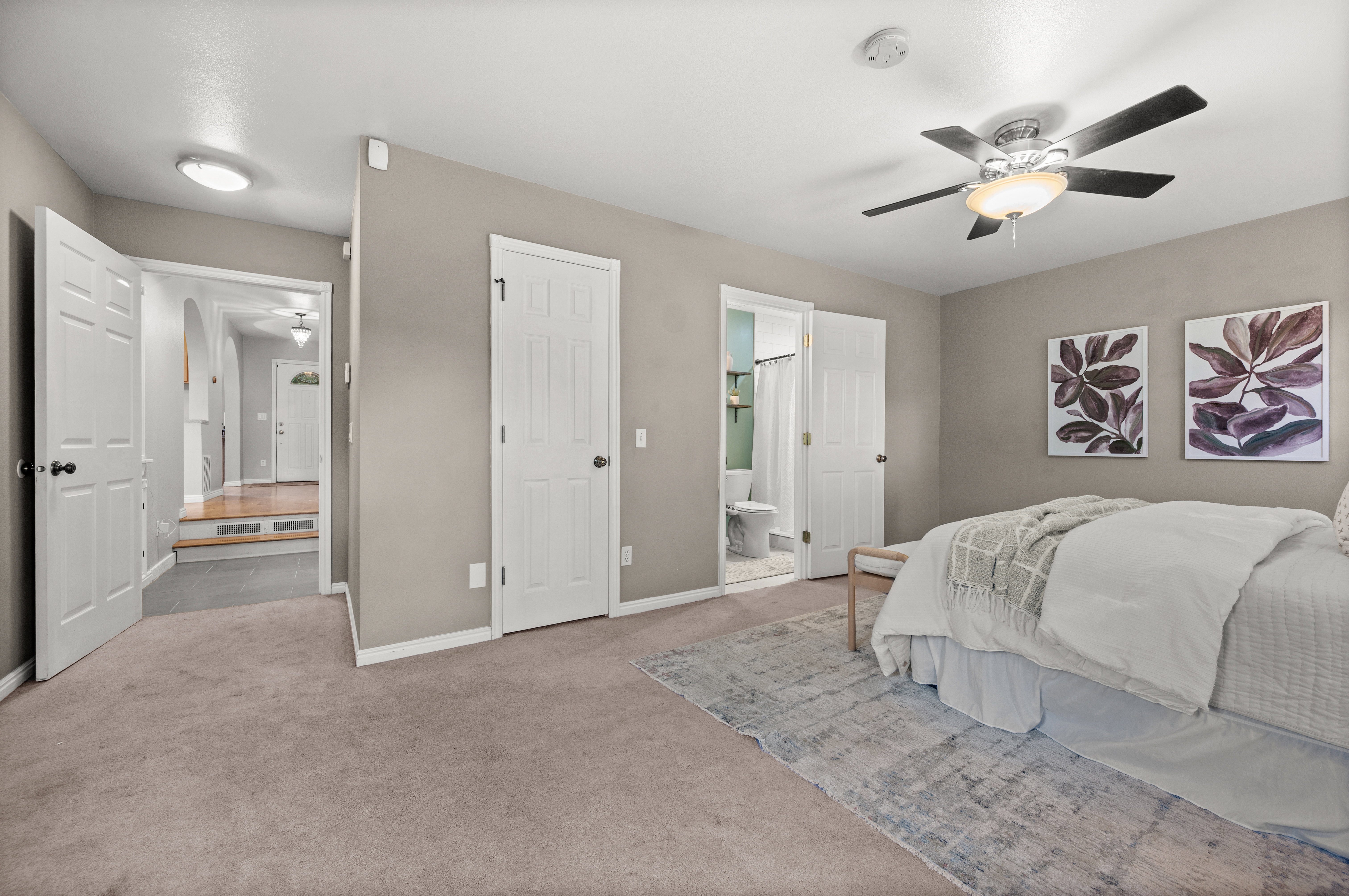 Carpeted bedroom featuring a ceiling fan with integrated lighting, a panel door leading to an en-suite bathroom, and a second panel door providing access to the hallway