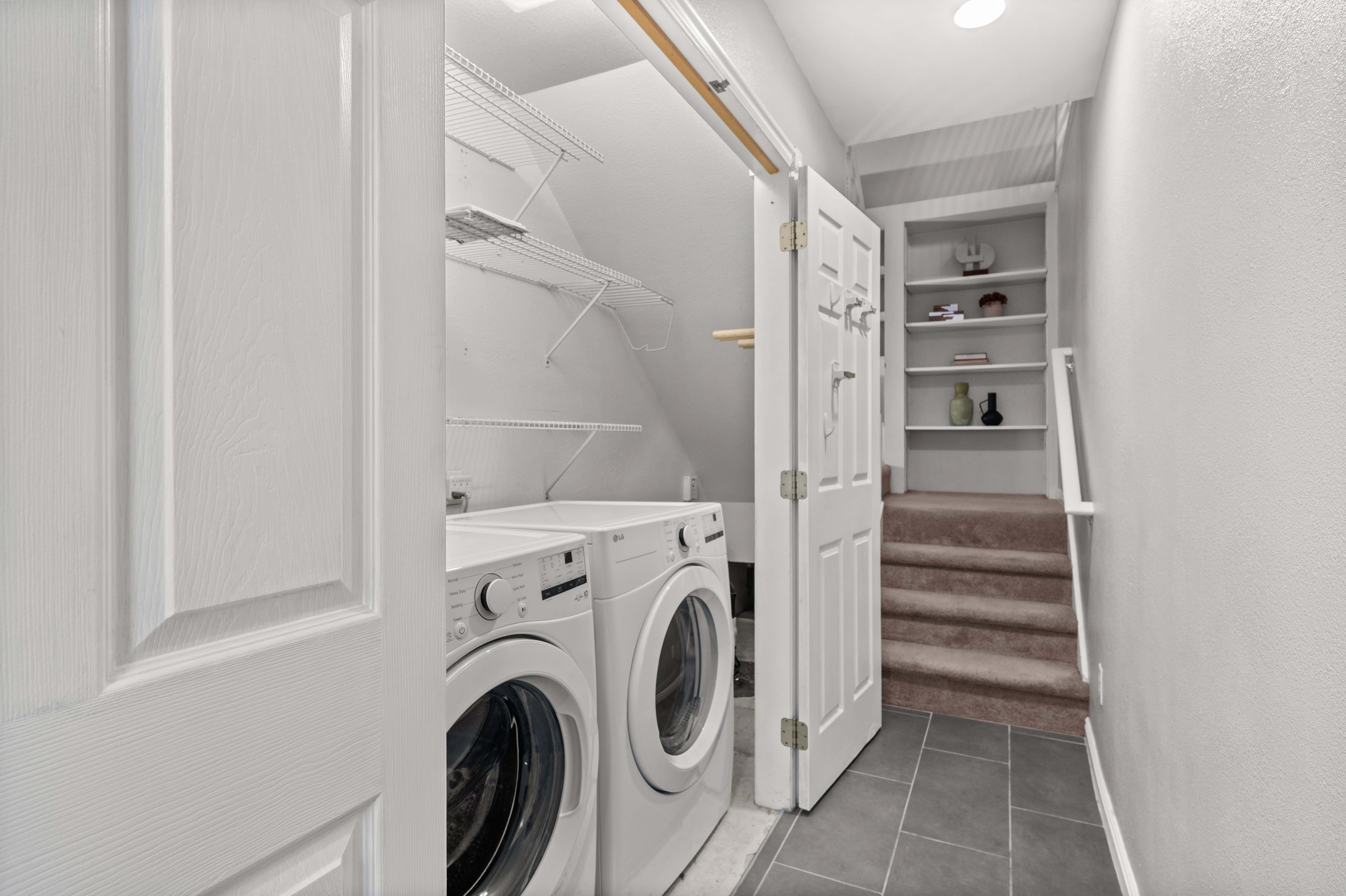Compact laundry area featuring front-loading appliances and wire shelving