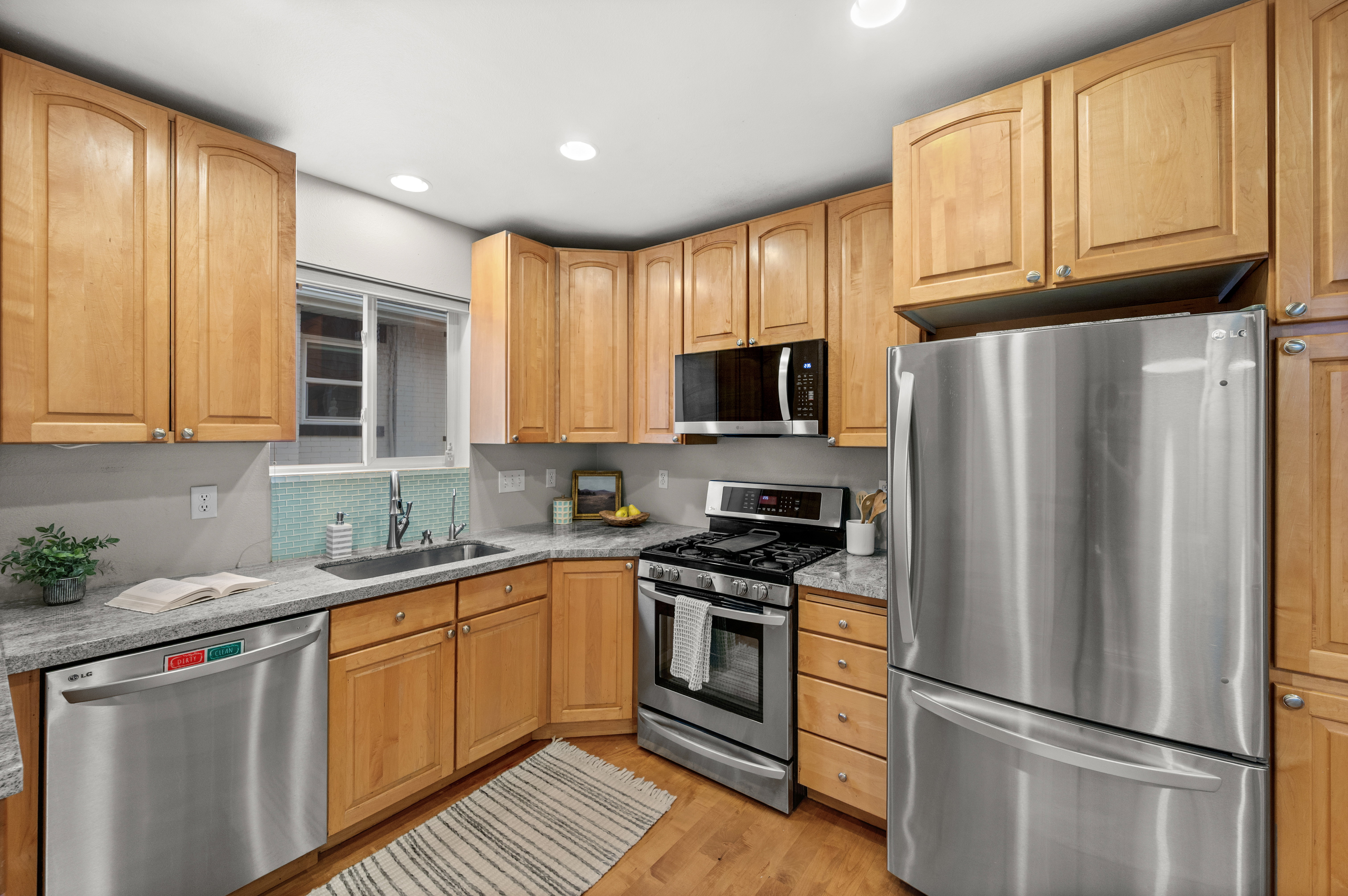 Kitchen featuring light wood cabinetry, granite-style countertops, stainless steel appliances, and a tiled backsplash