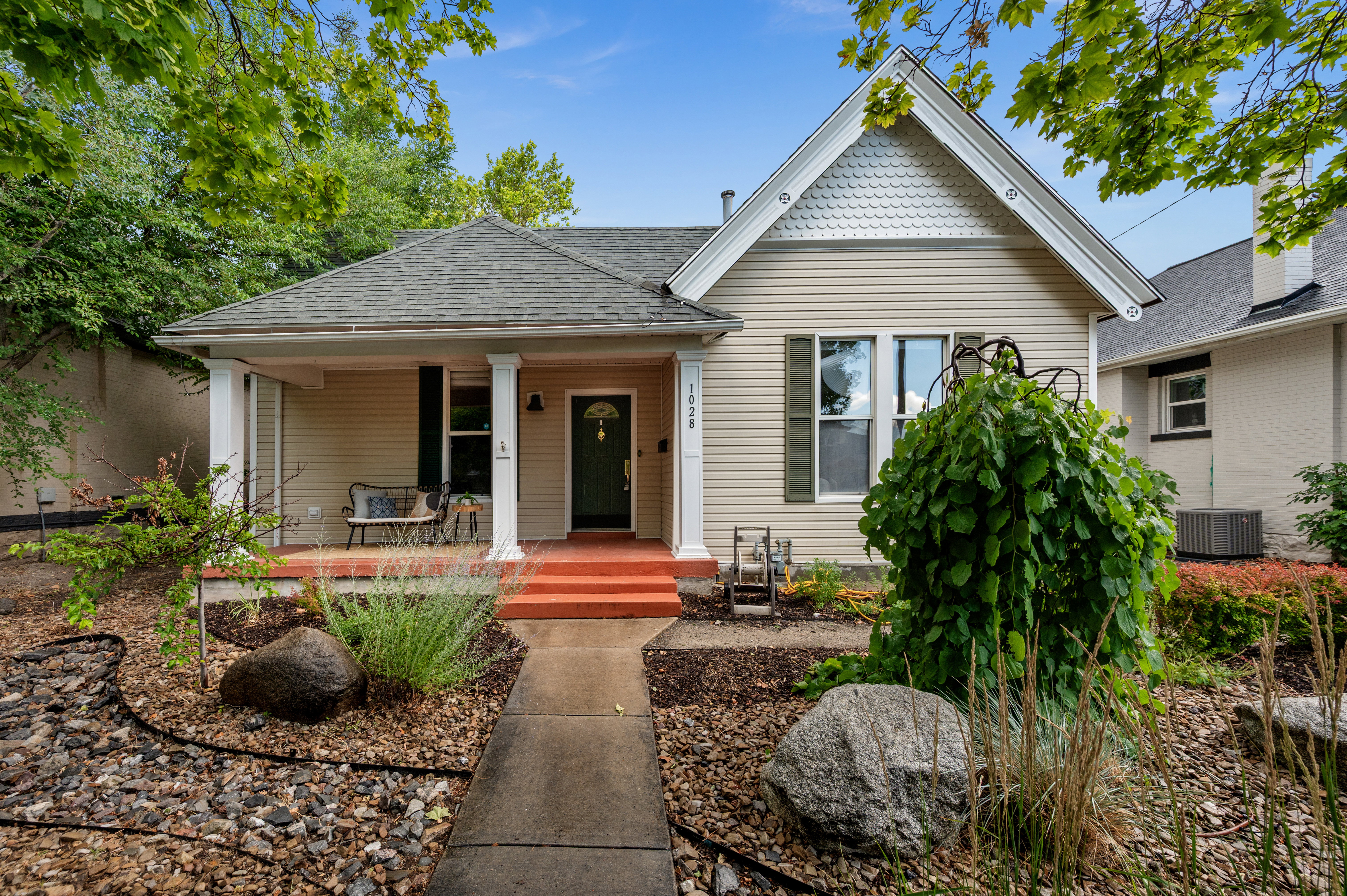 Charming bungalow exterior featuring tan siding, a covered front porch with white columns, and a dark green entry door