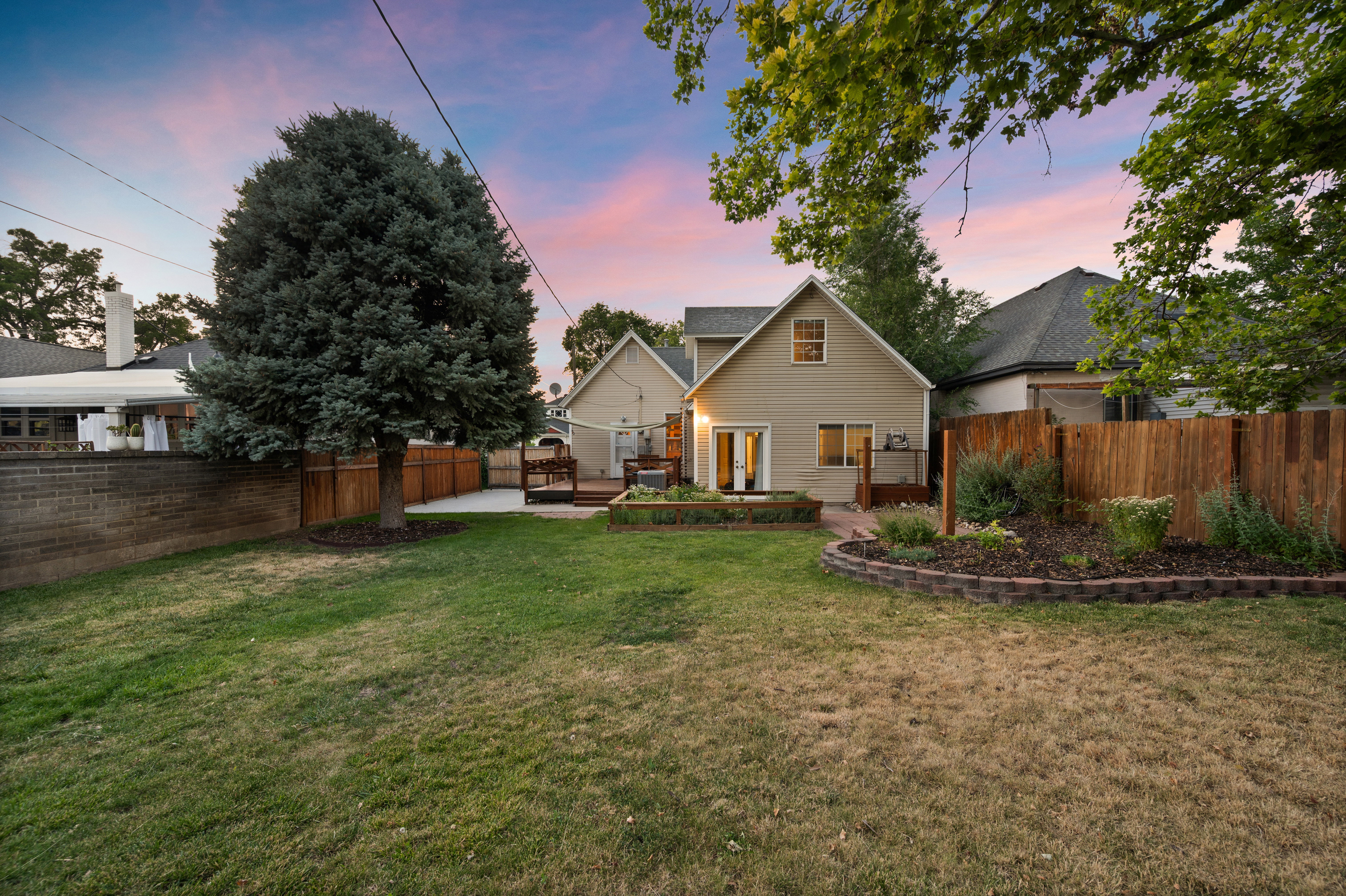 Expansive backyard featuring a mature evergreen tree, wood fencing, and a brick retaining wall