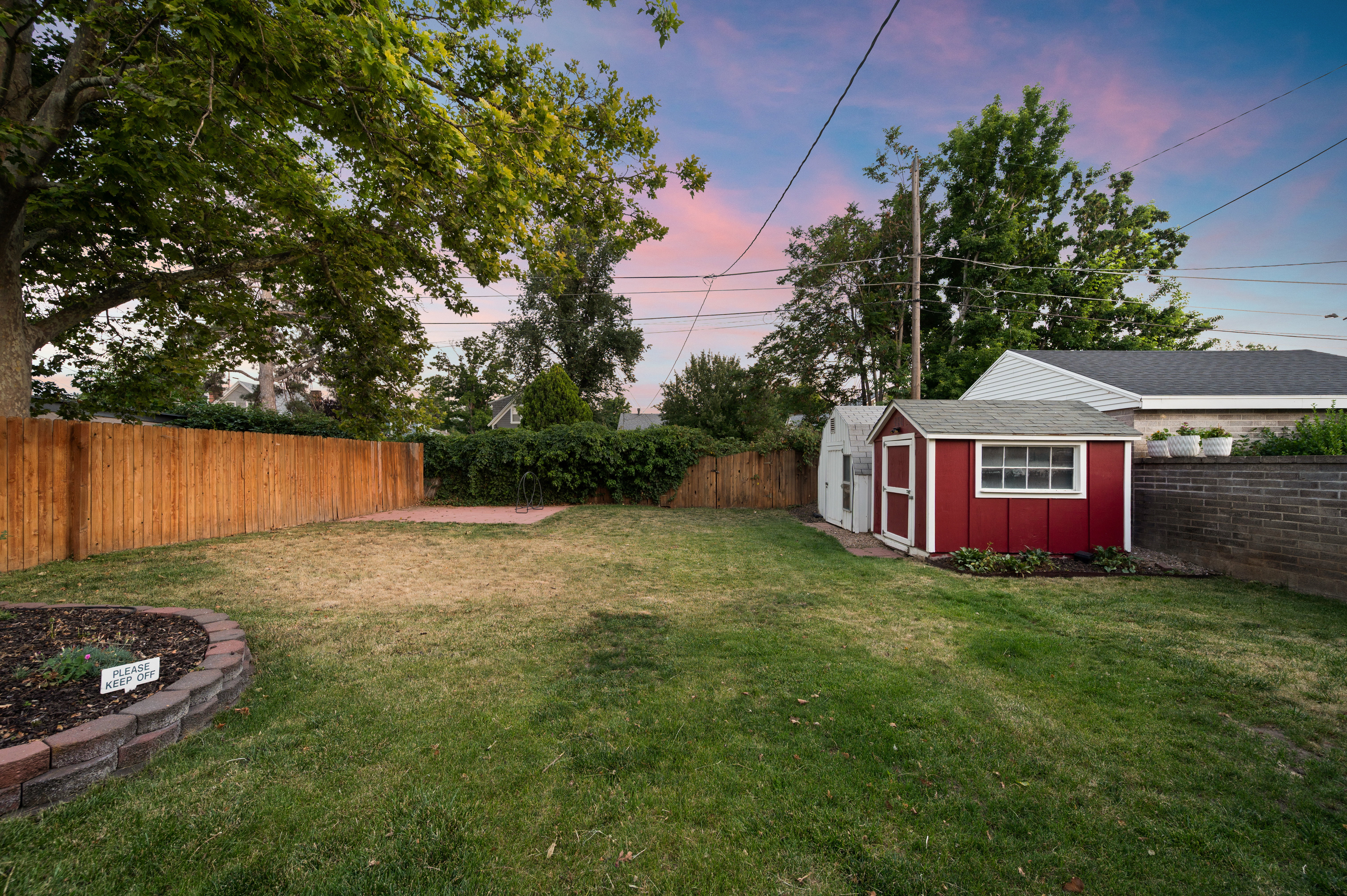 Expansive backyard featuring a red storage shed with white trim, a second white storage shed, and a wooden privacy fence