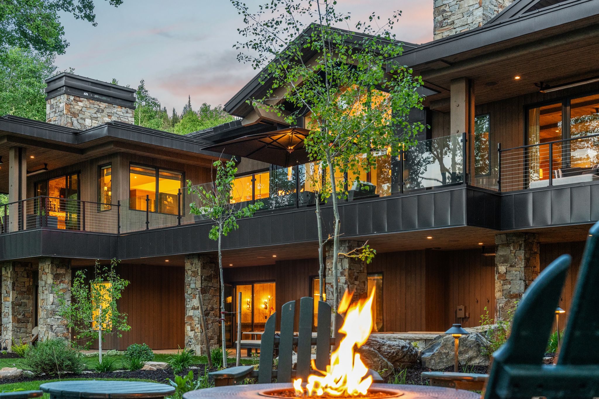 Expansive multi-level property featuring stone and wood-panel exterior, multiple balconies with glass railings, and an outdoor fire pit area