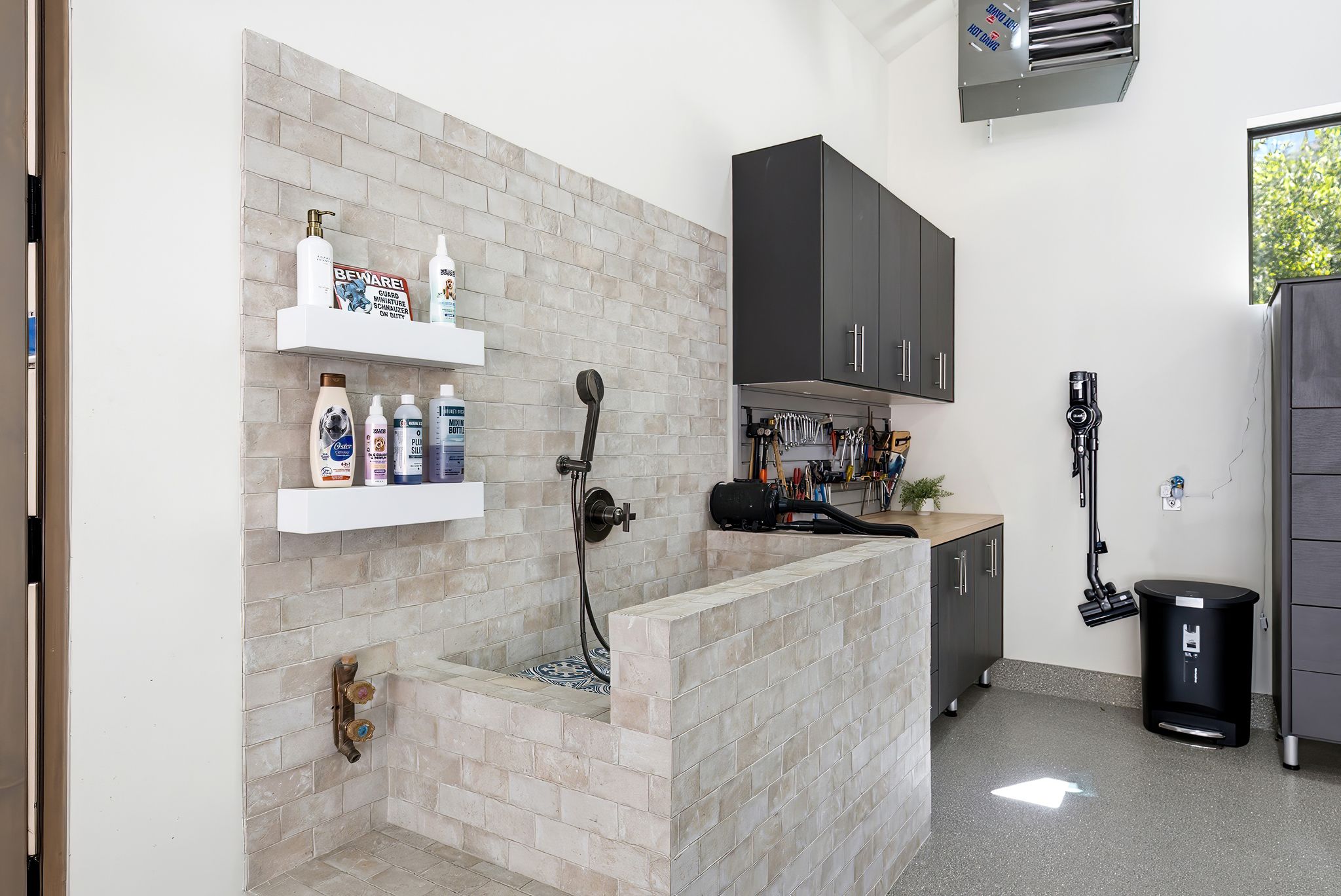 Dedicated utility room featuring a tiled pet washing station with handheld shower, built-in cabinetry, a wood-finish countertop, and a wall-mounted heater