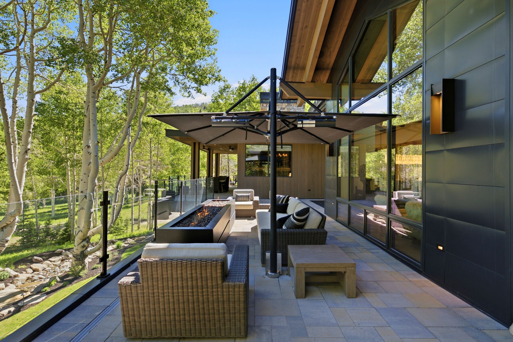 Spacious outdoor patio featuring a built-in linear fire pit, glass railing, and paver flooring