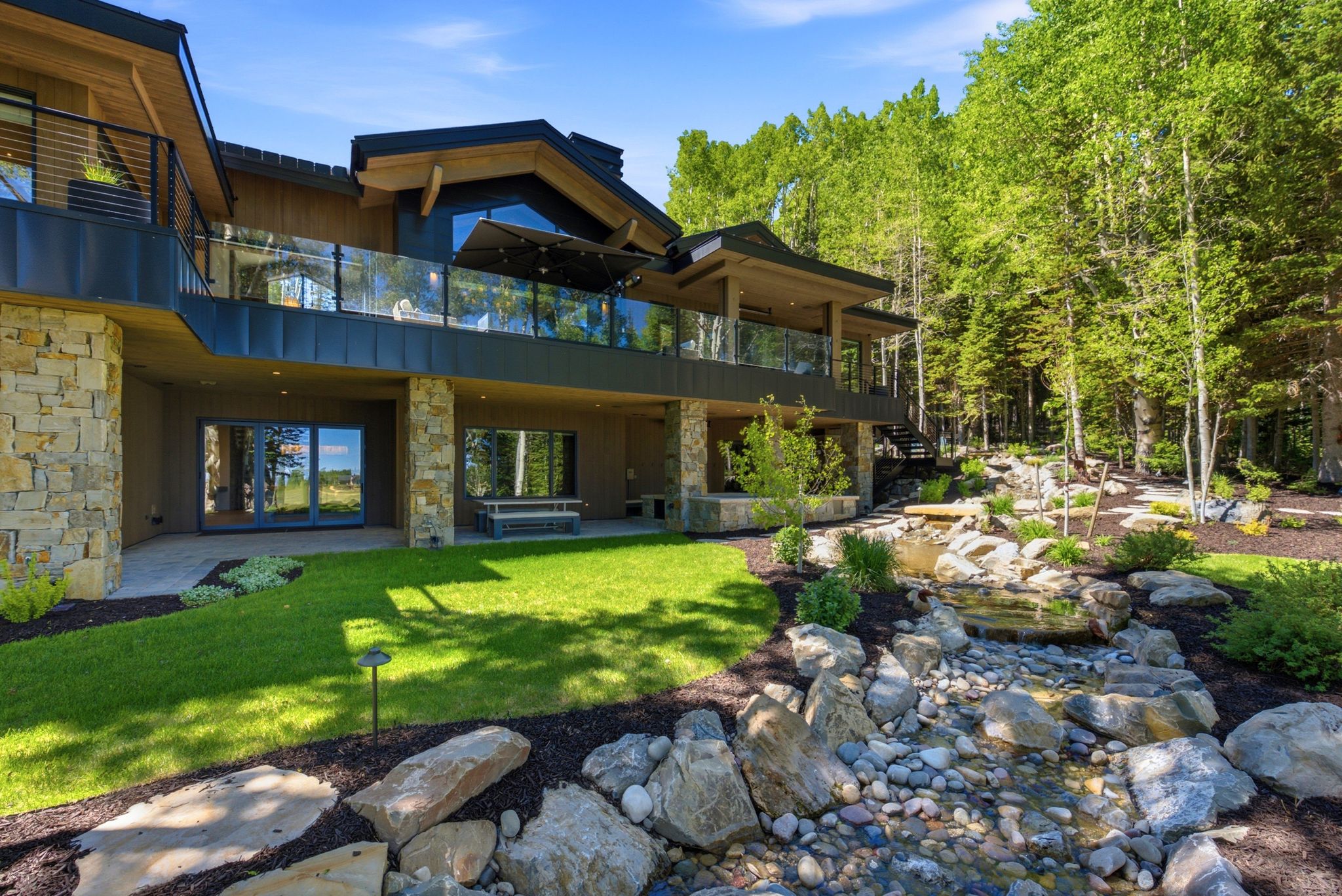 Multi-level residence featuring stacked stone pillars, wood-paneled siding, and expansive glass railings on the upper deck