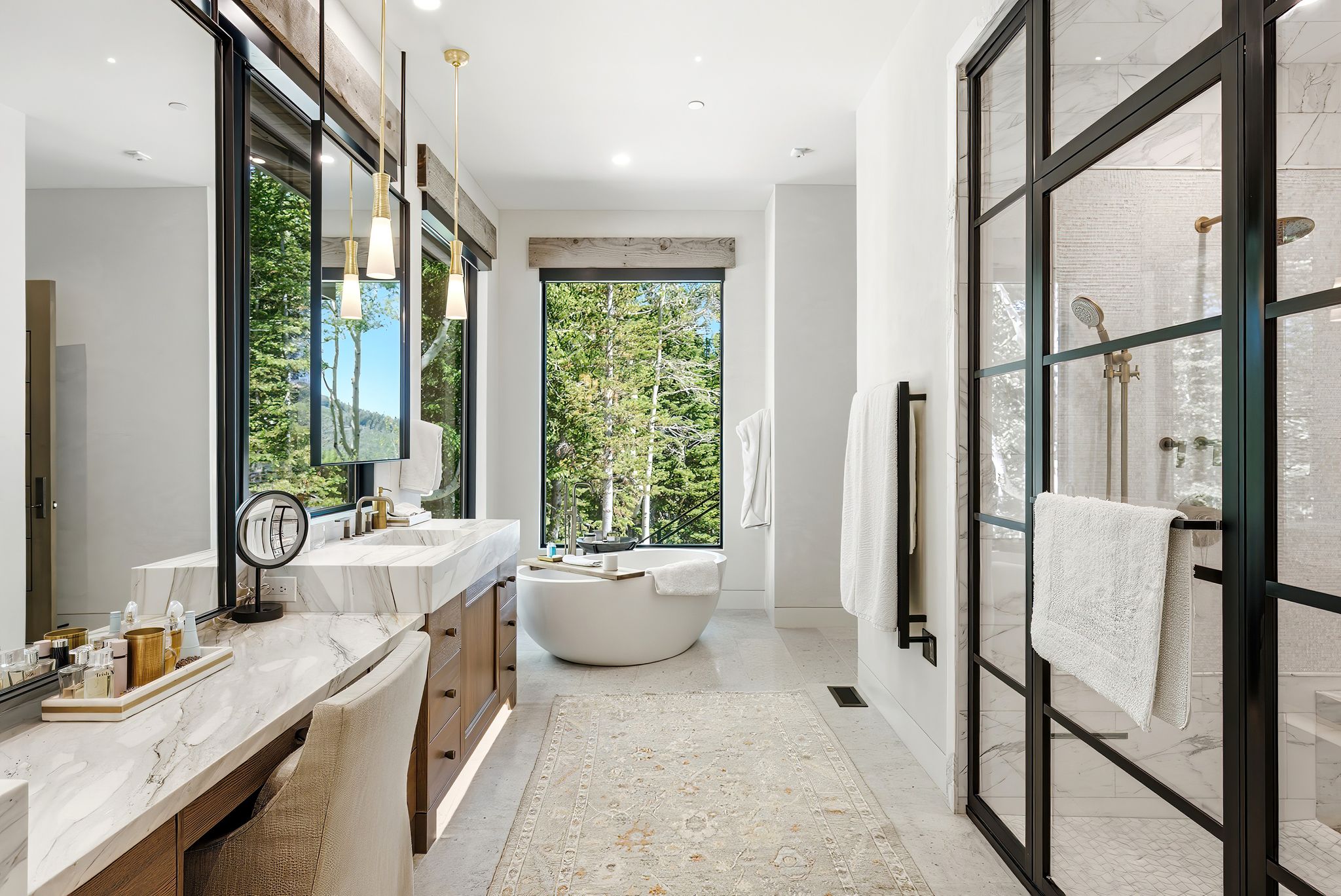Contemporary bathroom featuring a freestanding soaking tub, a multi-pane glass shower enclosure with brass fixtures, a double vanity with stone countertops, and large windows