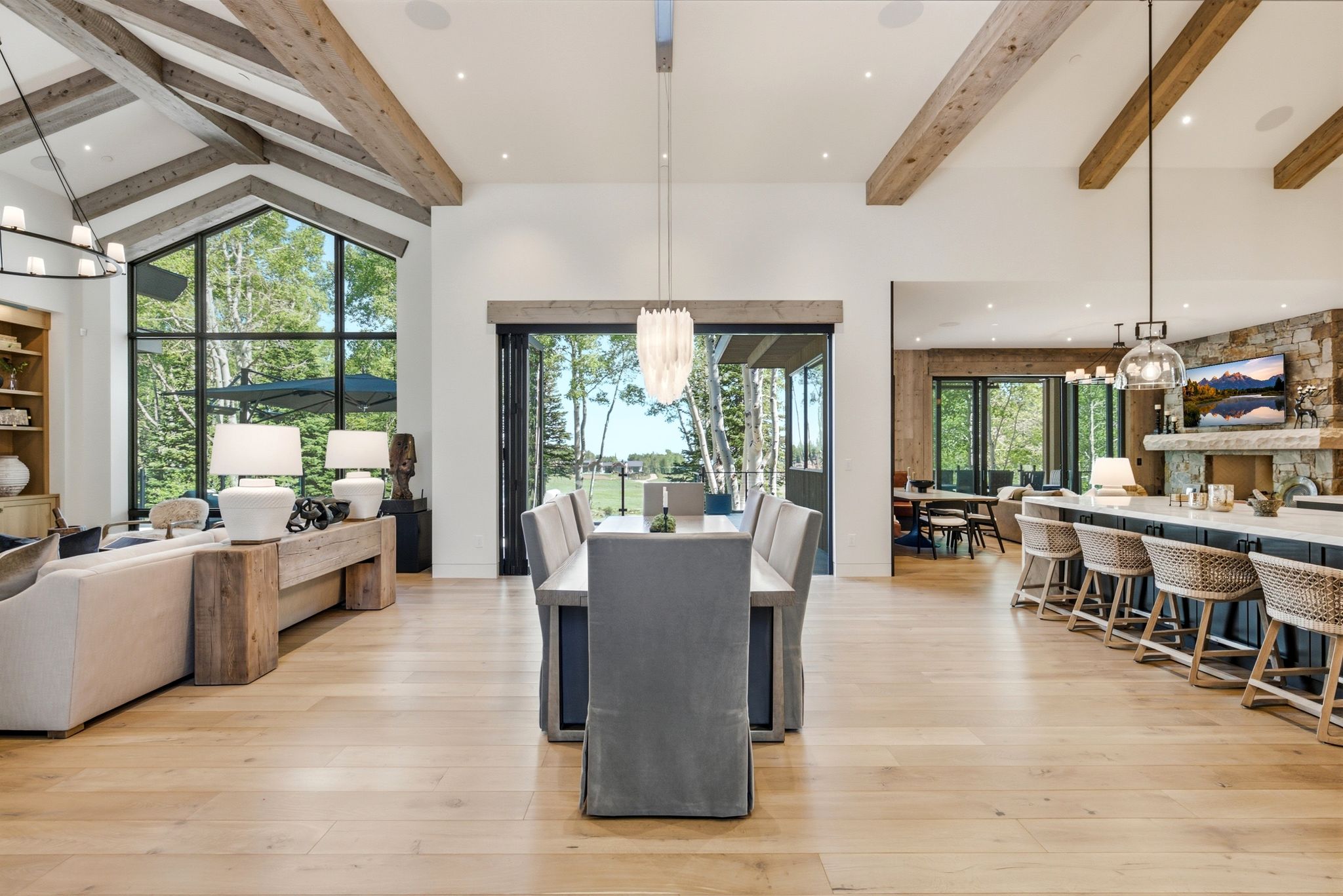 Great room featuring exposed wood ceiling beams, wide plank wood-finish flooring, and a dining area with direct access to an outdoor space via folding glass doors