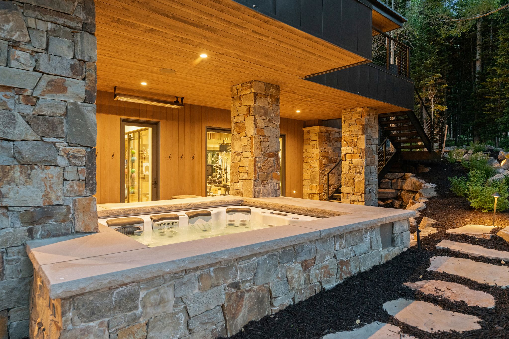 Integrated outdoor spa with stone surround, complemented by stone columns and a wood-paneled ceiling