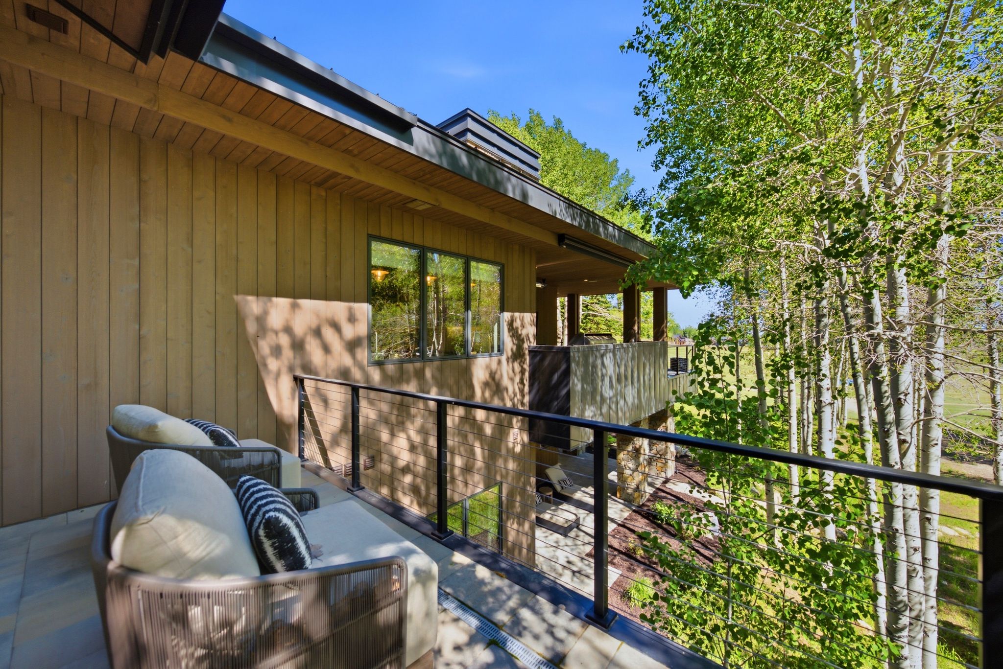 Expansive outdoor deck featuring wood-finish siding, a contemporary cable railing system, and large windows reflecting surrounding greenery