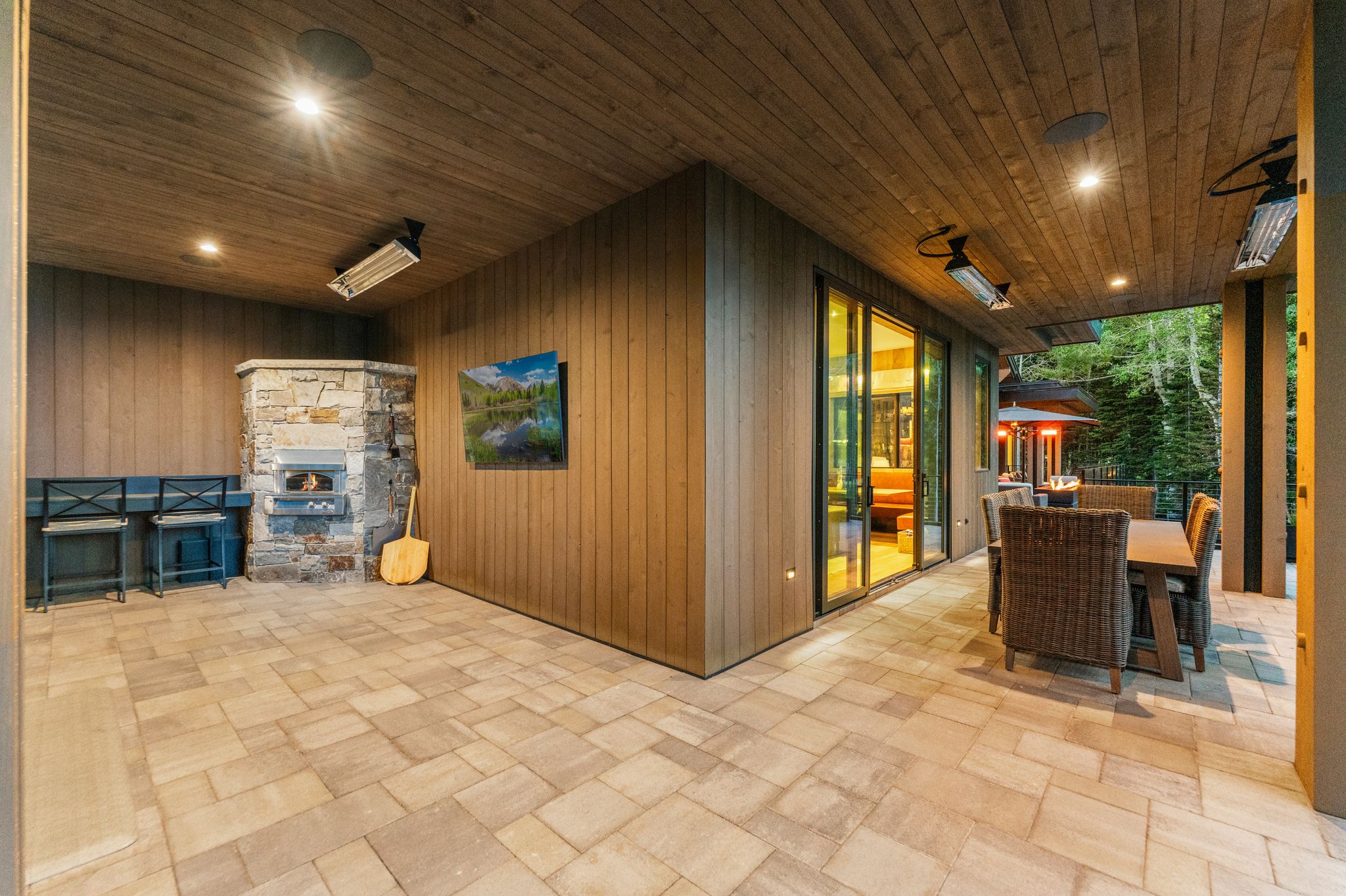 Expansive covered patio featuring a stone-clad pizza oven, recessed lighting, wood plank ceiling, and large format paver flooring