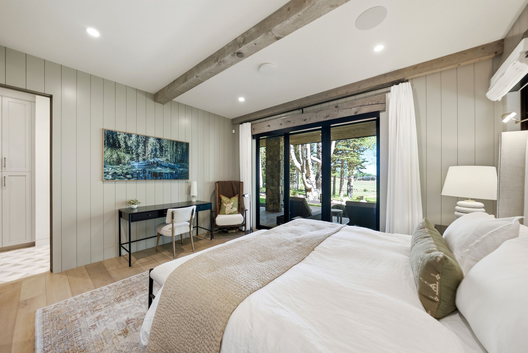 Spacious bedroom featuring light wood-finish flooring, exposed ceiling beams, and a board and batten accent wall