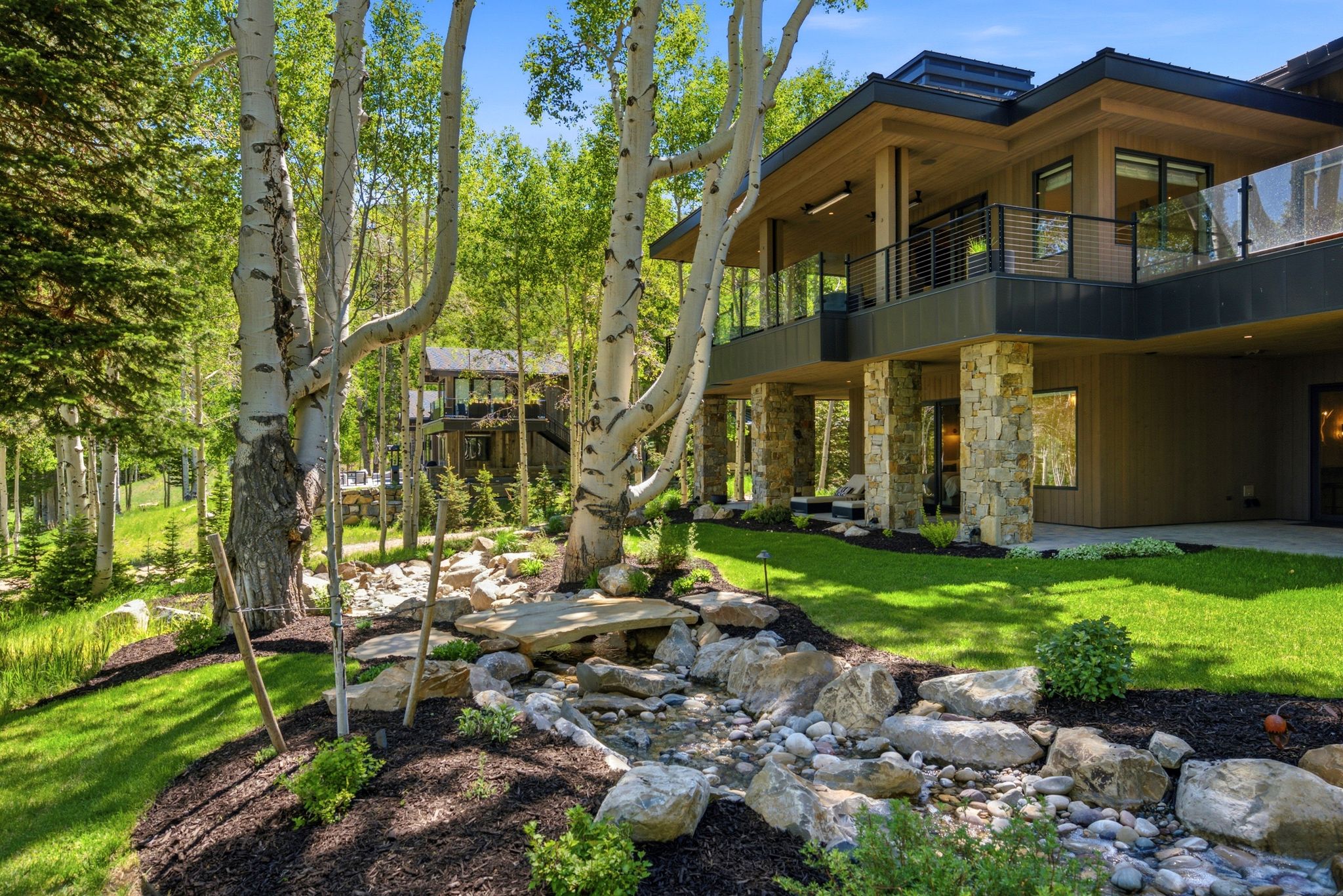 Modern multi-level exterior with stone-clad columns and a glass-paneled upper deck
