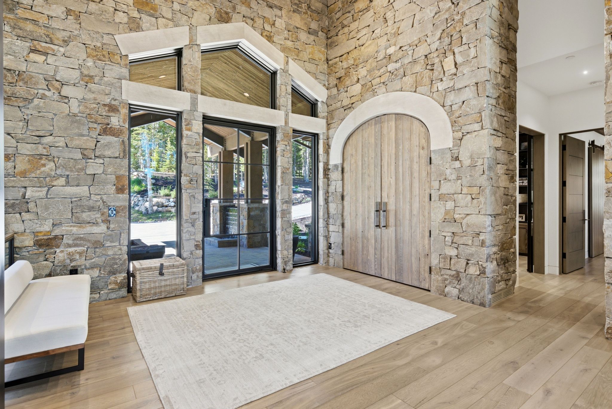 Grand entry featuring extensive stone wall cladding, large arched wood entry doors, and expansive black-framed windows