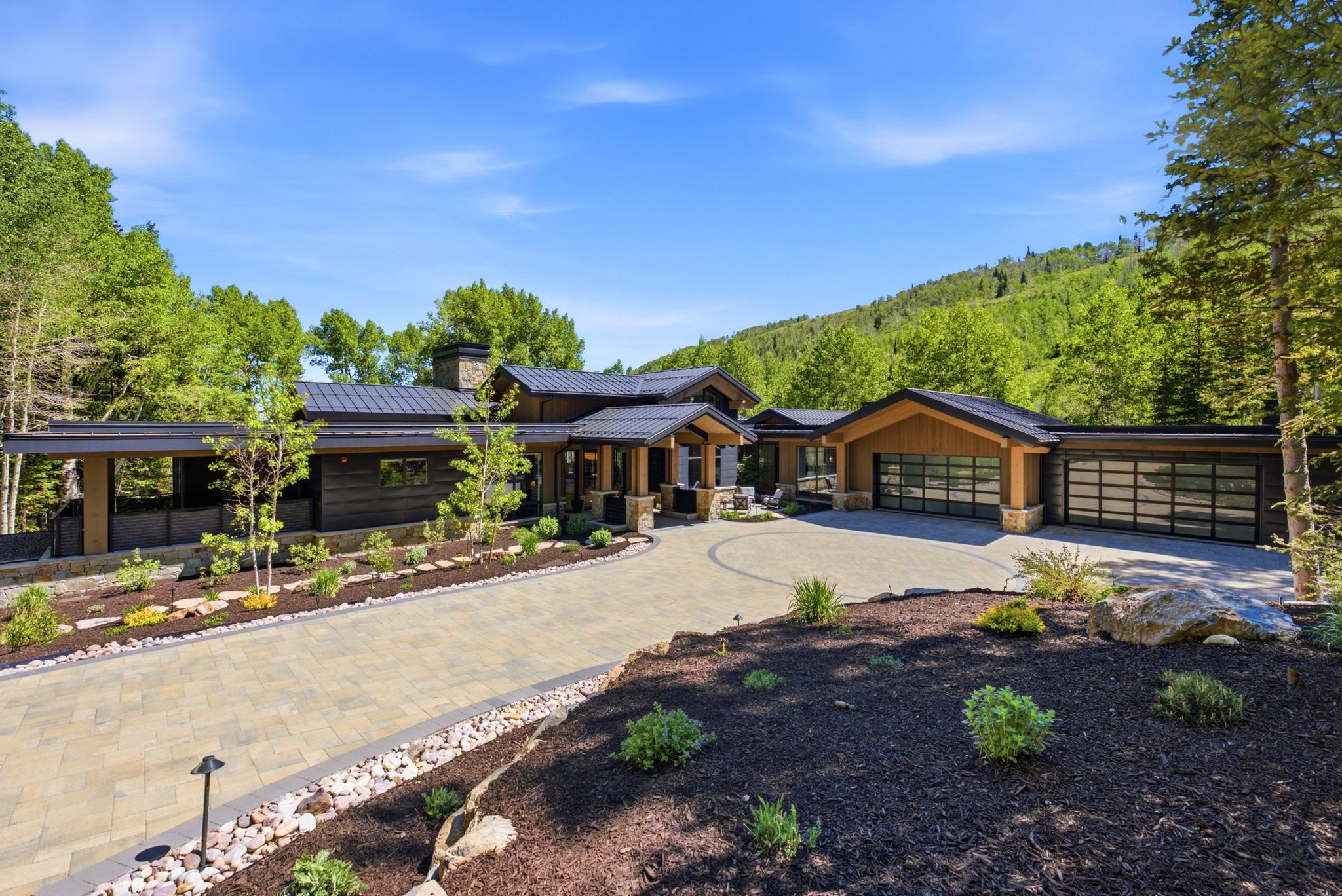 Contemporary residence featuring a paver driveway, stone accents, and a dark metal roof