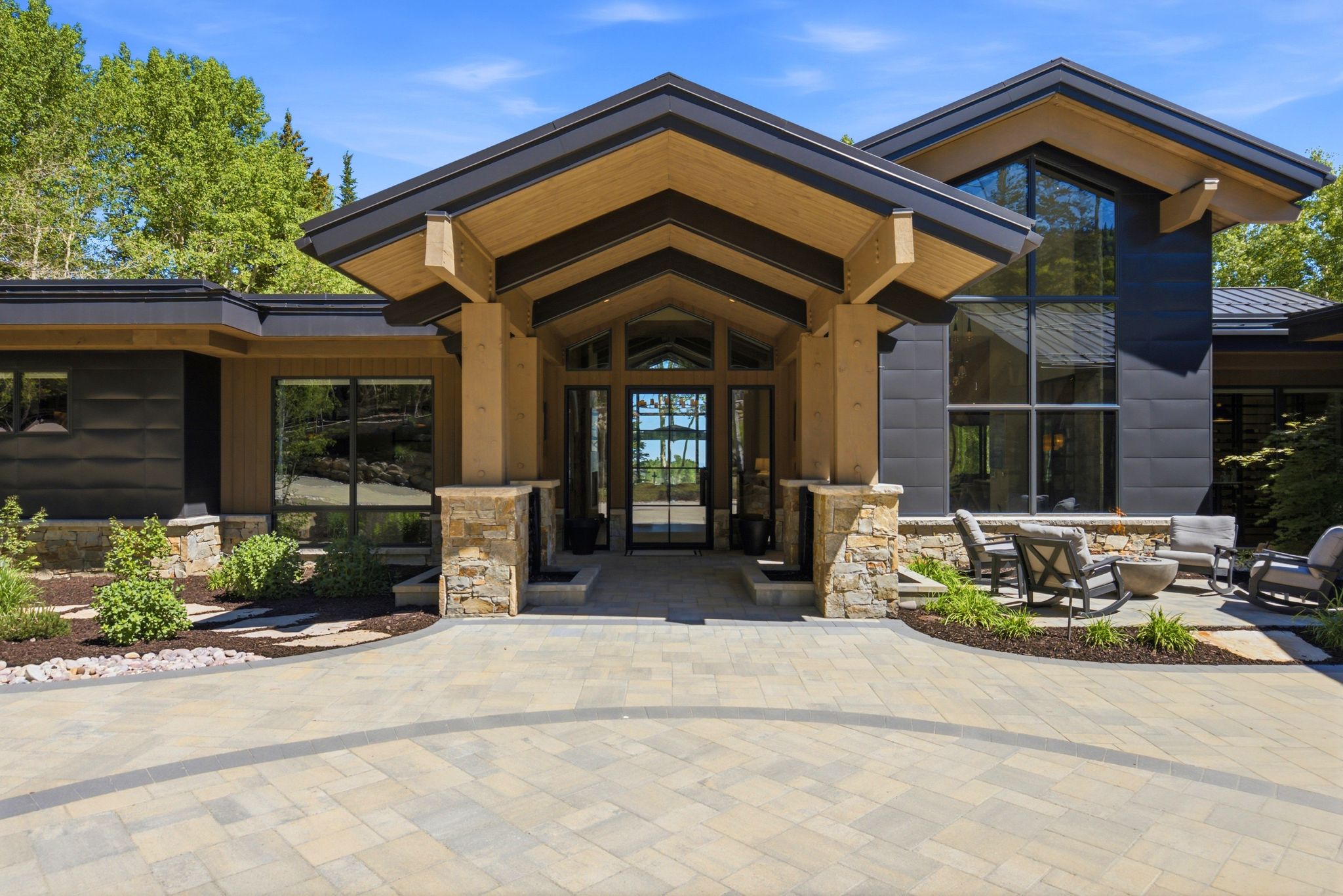 Contemporary architecture featuring a grand entry with wood beam accents, expansive glass doors, stone column bases, and a stone-clad exterior with large windows
