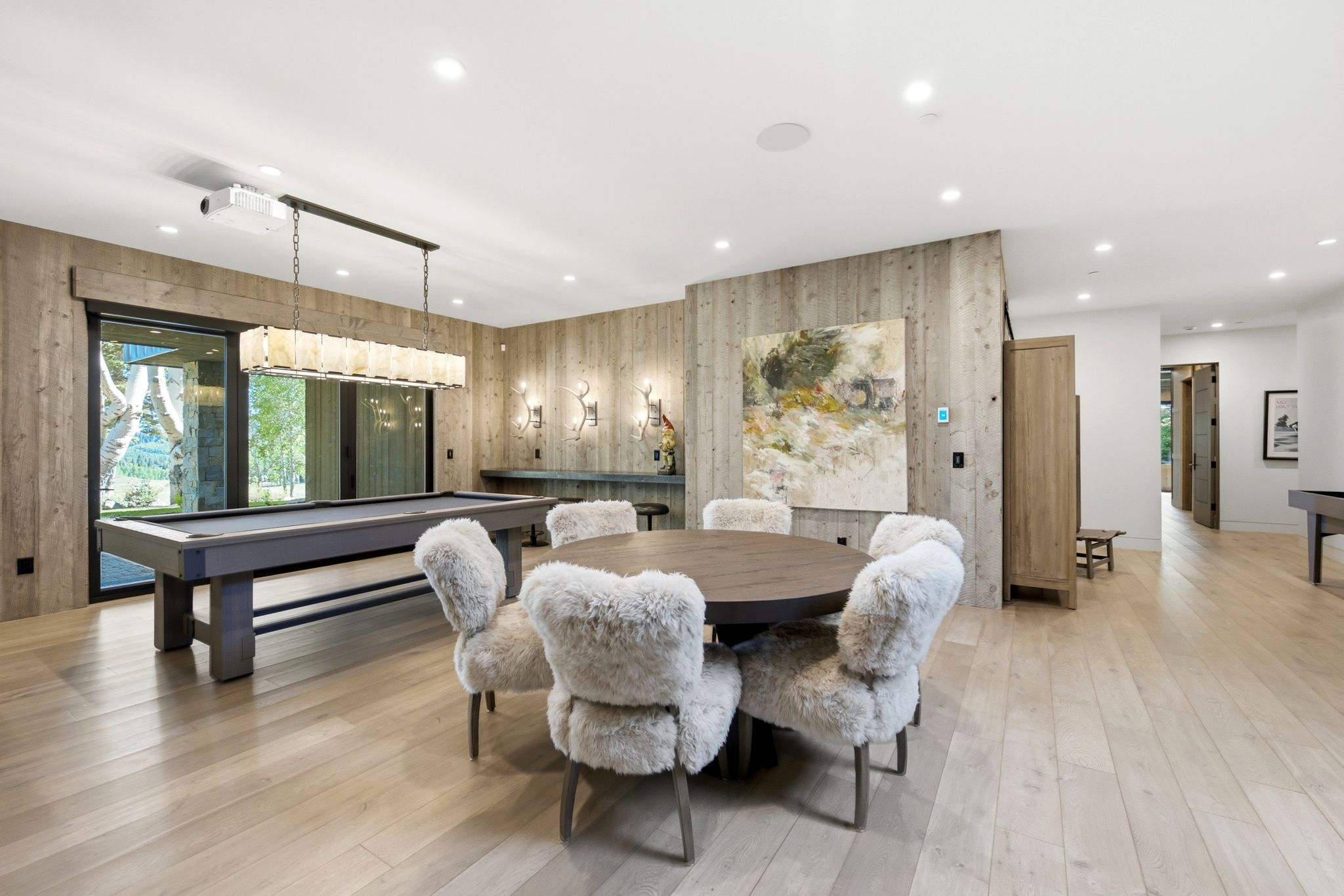 Spacious entertainment area featuring light wood-finish flooring, recessed lighting, and accent walls with vertical wood paneling