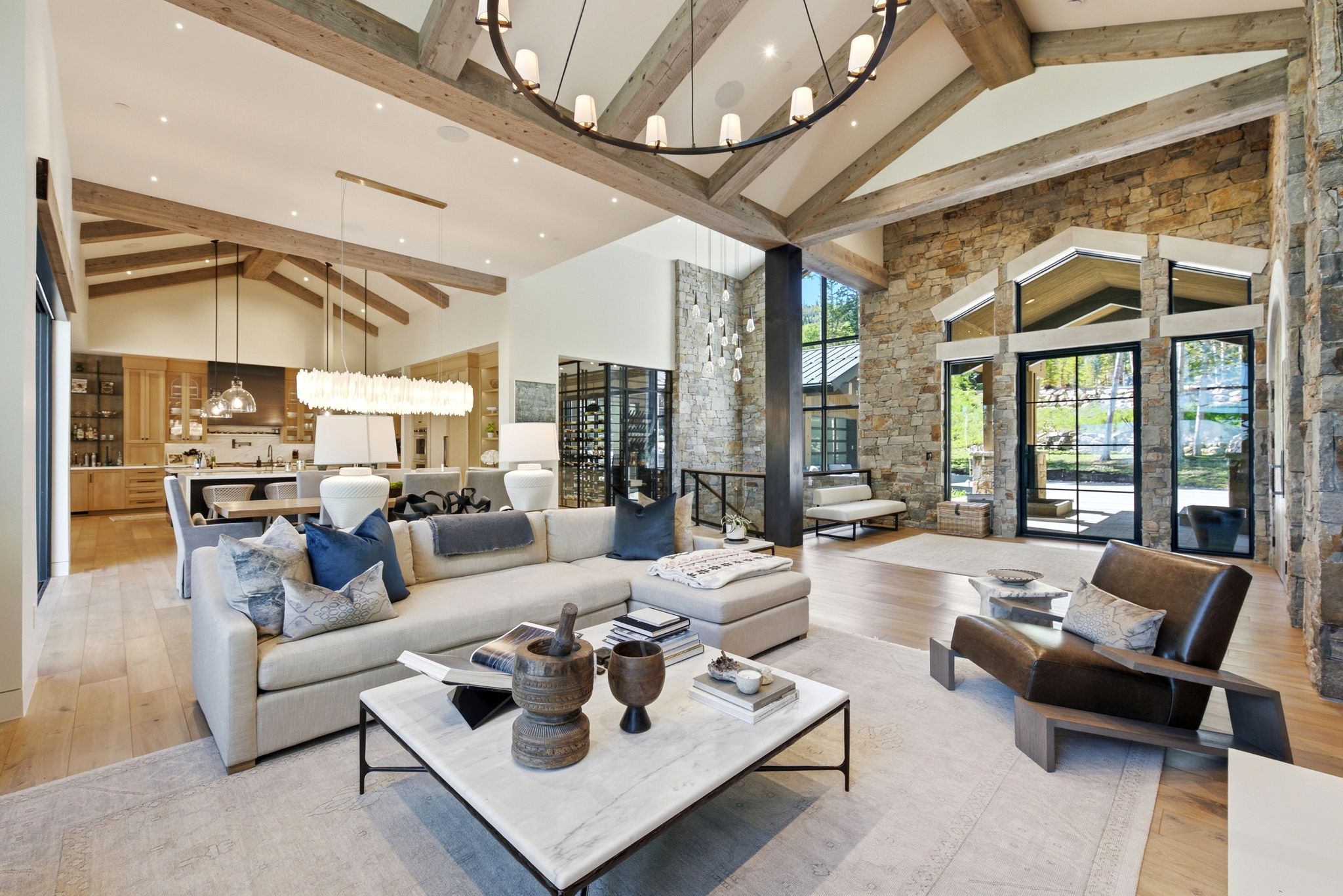 Spacious living area featuring a vaulted ceiling with exposed wood beams, stone accent walls, wood-finish flooring, and expansive windows