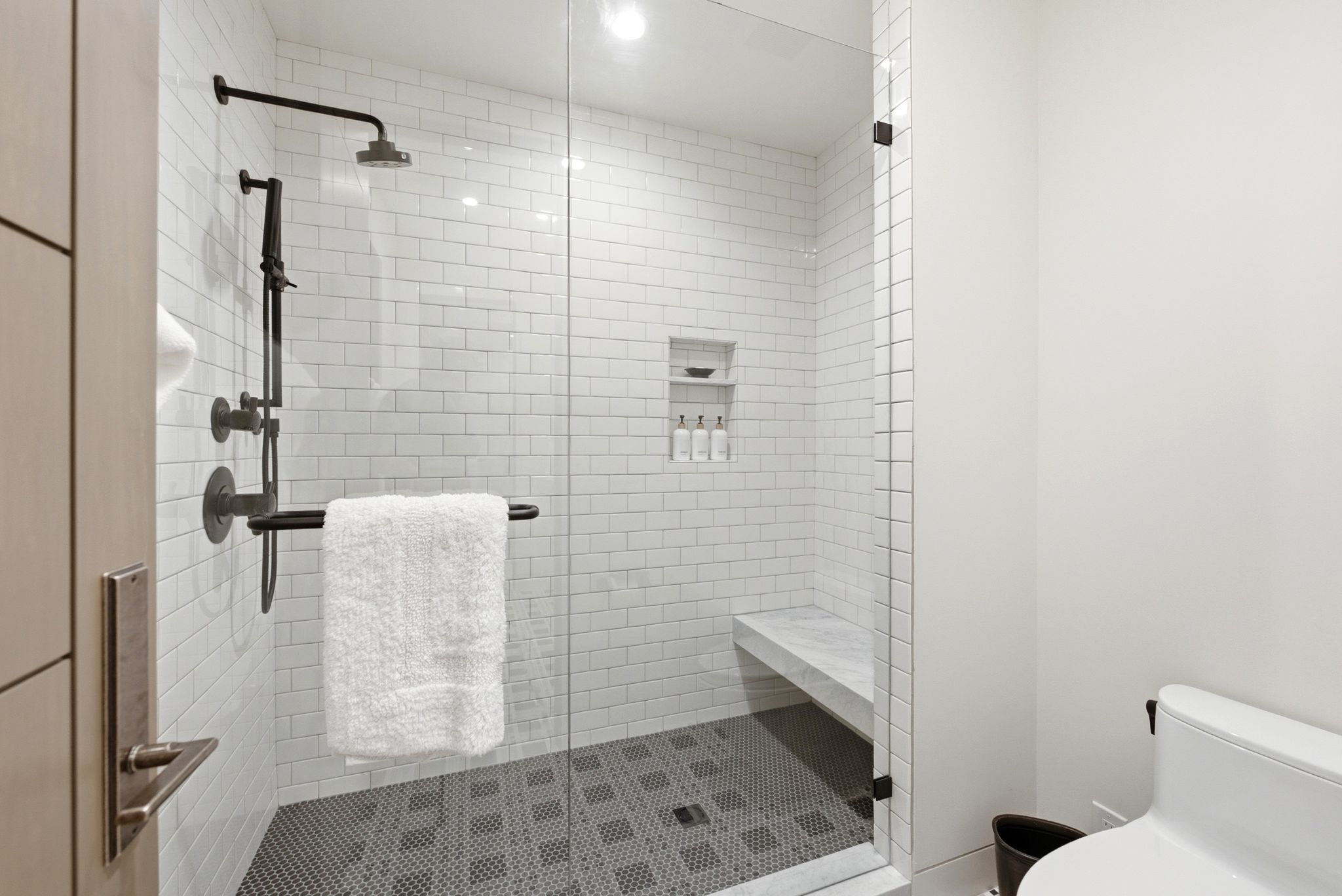 Walk-in shower featuring a glass enclosure, subway tile surround, dark penny tile flooring, built-in shelving, and a shower bench