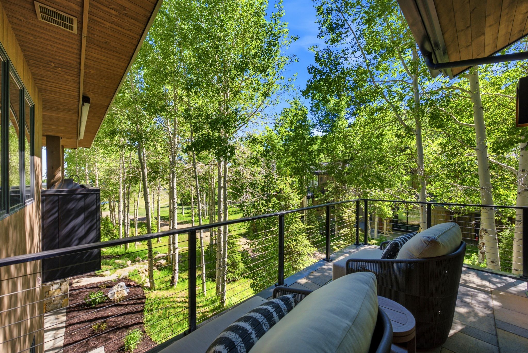 Outdoor deck featuring a cable railing system, wood-finish soffit, and tree-lined surroundings