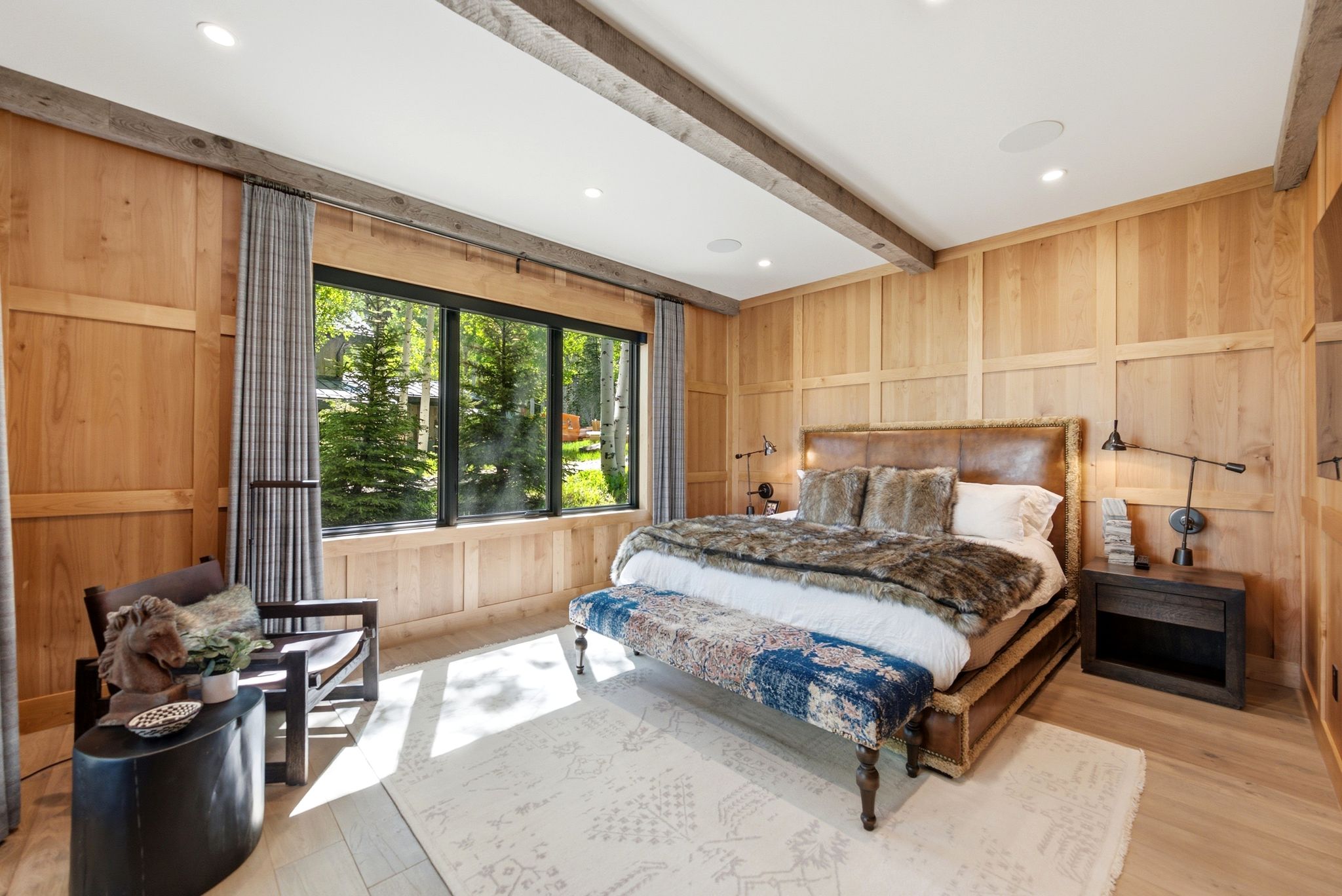 Wood paneling throughout, featuring a broad window with exterior greenery, recessed ceiling lighting, and exposed ceiling beams