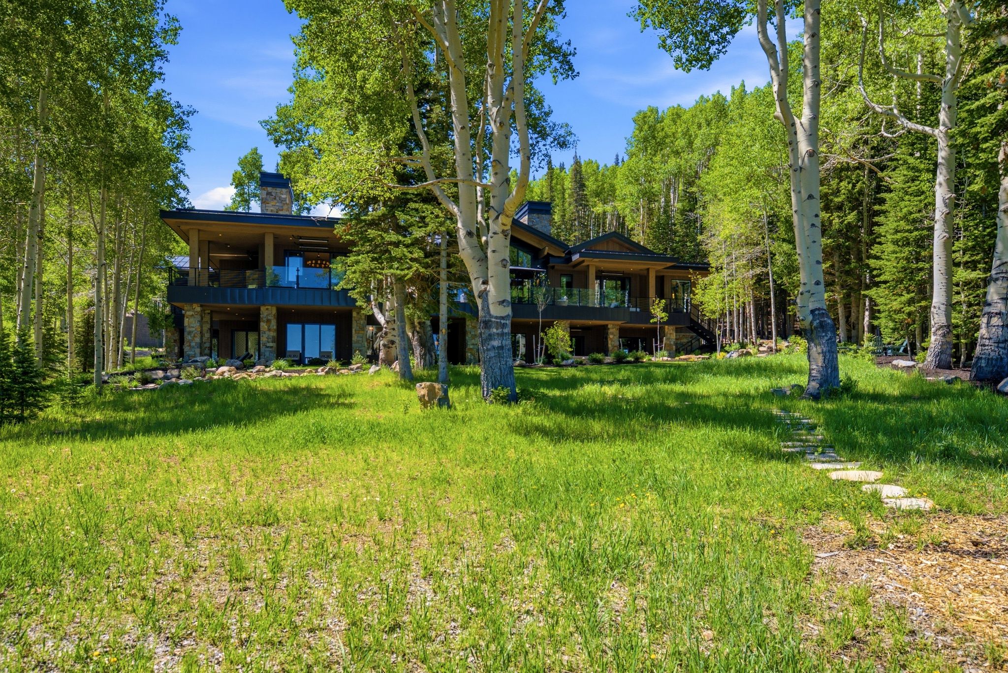 Modern mountain architecture with stone and wood siding, featuring multi-level balconies with glass railings