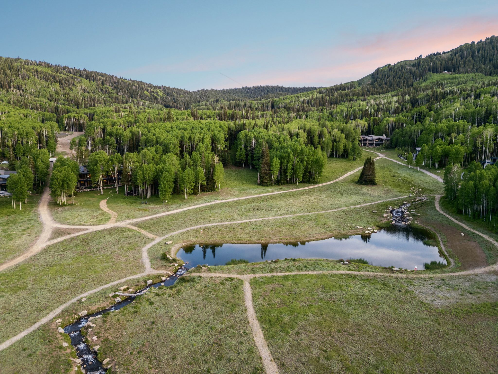 Lush mountain landscape featuring verdant trees, meandering pathways, and a tranquil pond with a flowing stream