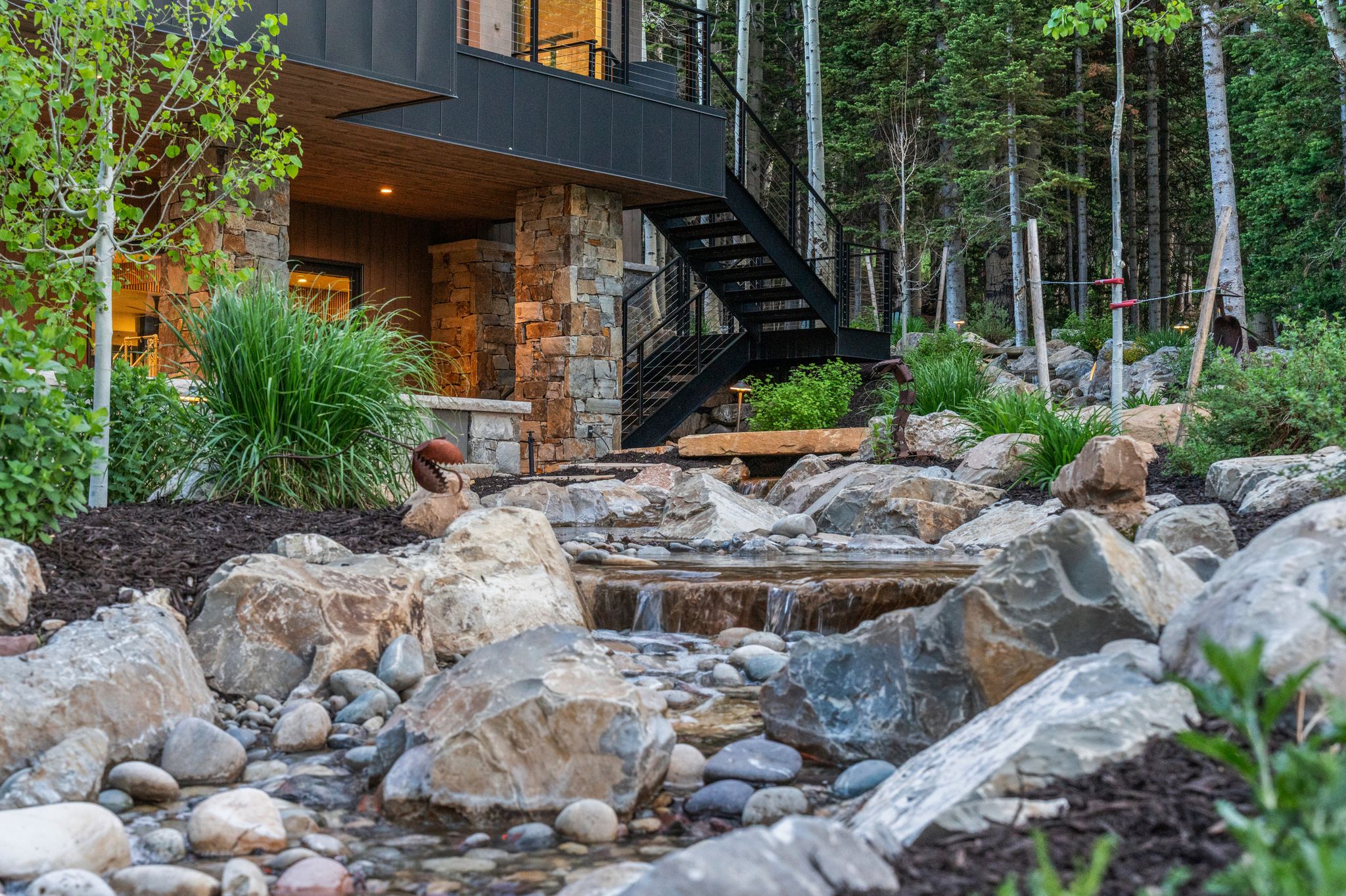 Tiered rock landscaping featuring a flowing water feature, mature trees, and natural plantings