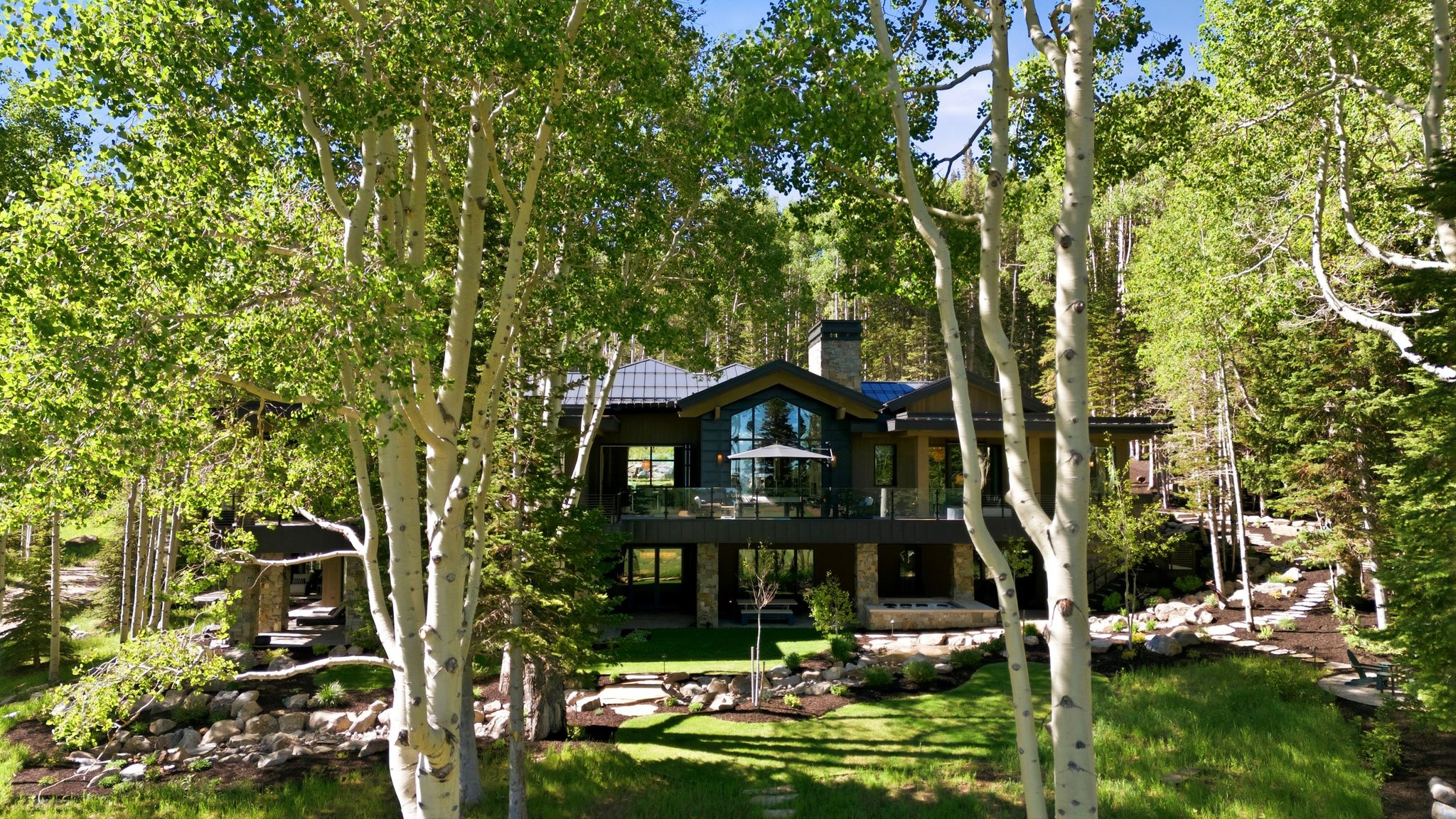 Stately multi-level residence with a dark-toned exterior and a stone foundation, set amidst mature trees