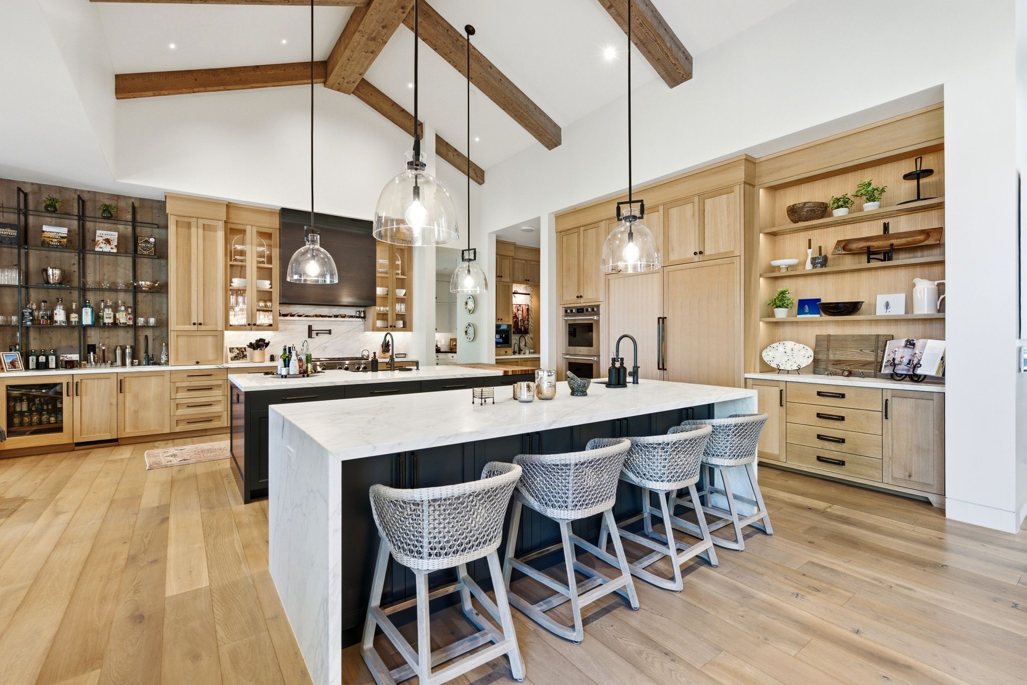 Open-concept kitchen featuring vaulted ceilings with exposed wood beams, wood-finish flooring, two large kitchen islands with stone countertops, and integrated appliances