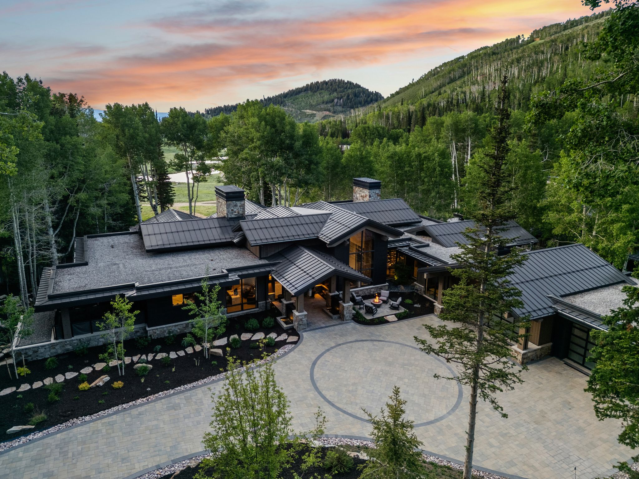 Expansive contemporary residence featuring multiple rooflines, stone and dark-toned siding, and a large circular driveway with paver accents