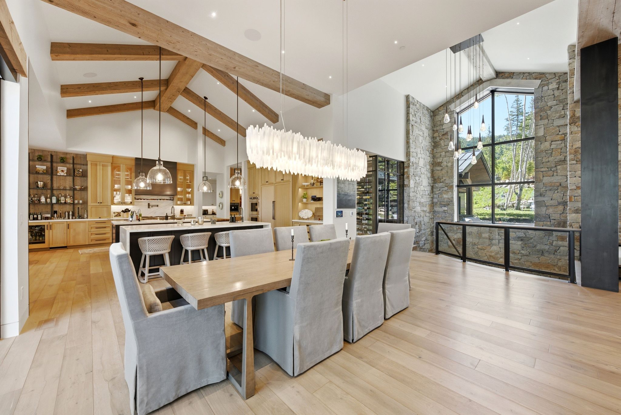 Spacious open-concept living area featuring a vaulted ceiling with exposed wood beams, light wood-finish flooring, and a stone accent wall