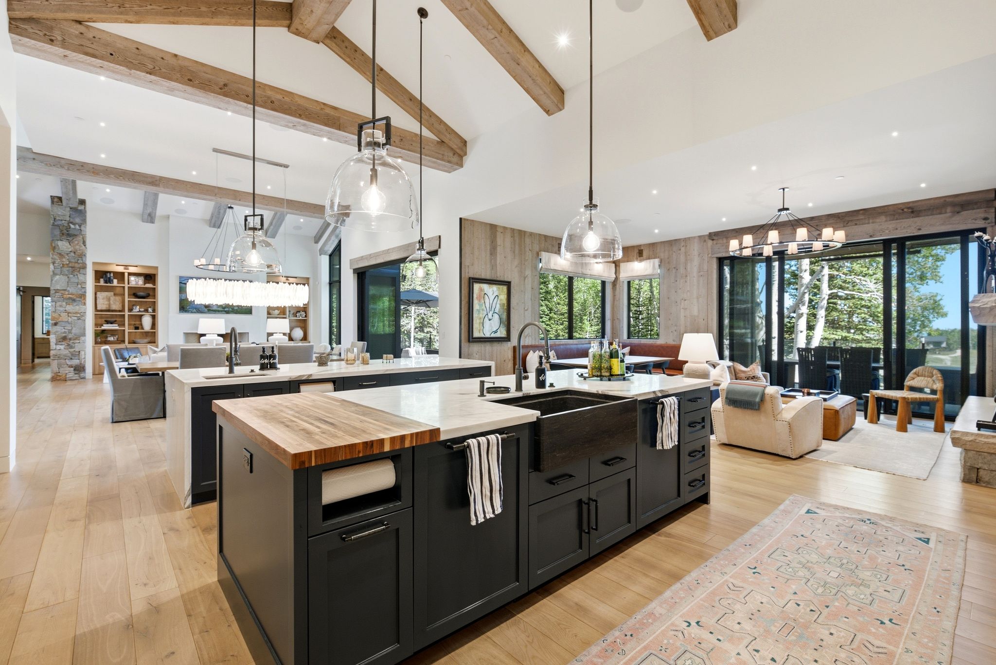 Open-concept kitchen featuring two large islands with stone and wood-finish countertops, a dark farmhouse sink, and pendant lighting